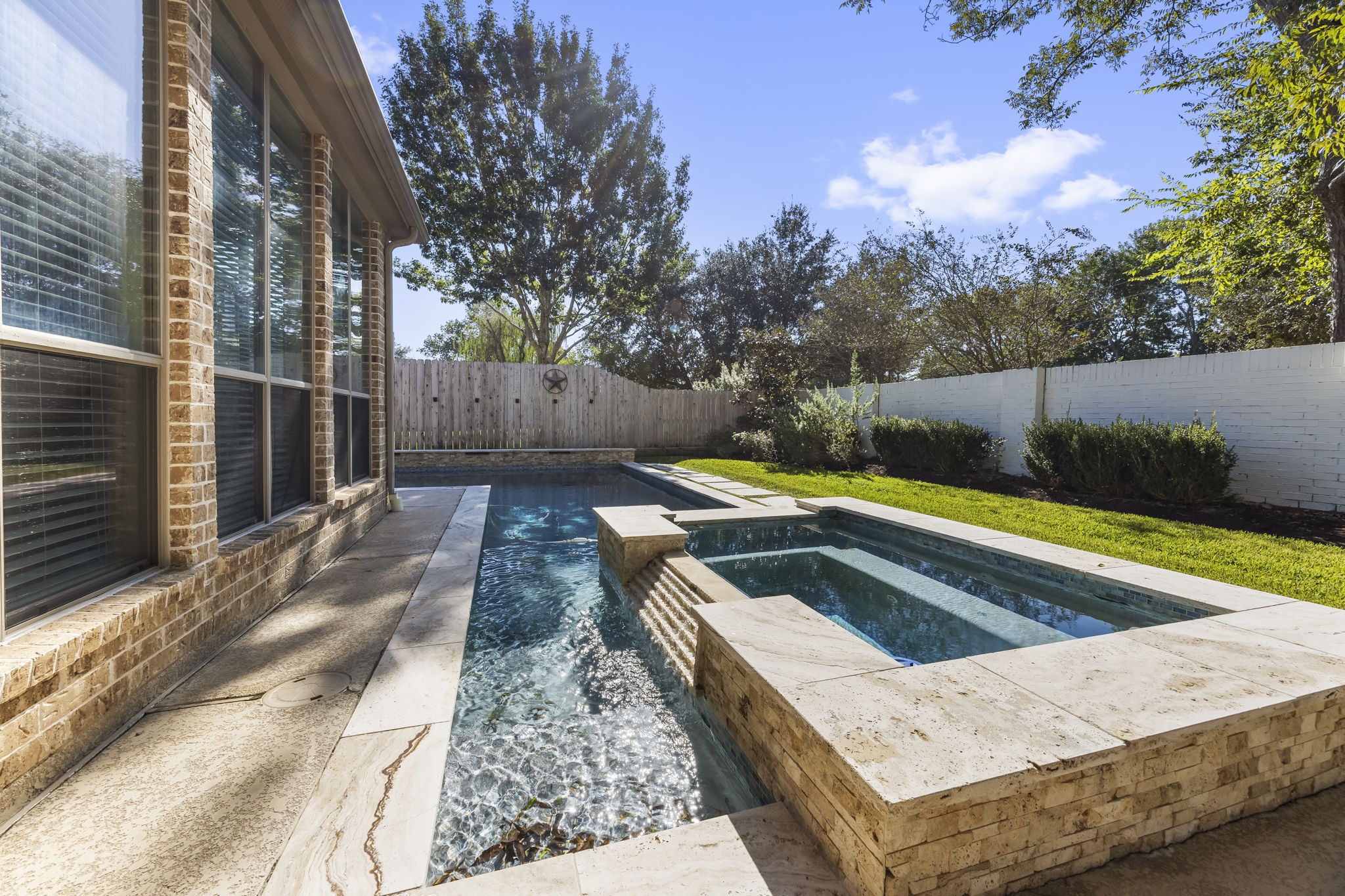 Beautifully designed pool with an elevated spa, cascading water feature, and elegant stone coping. Surrounded by mature trees and lush landscaping, this private backyard retreat offers the perfect setting to cool off, unwind, and enjoy the outdoors.