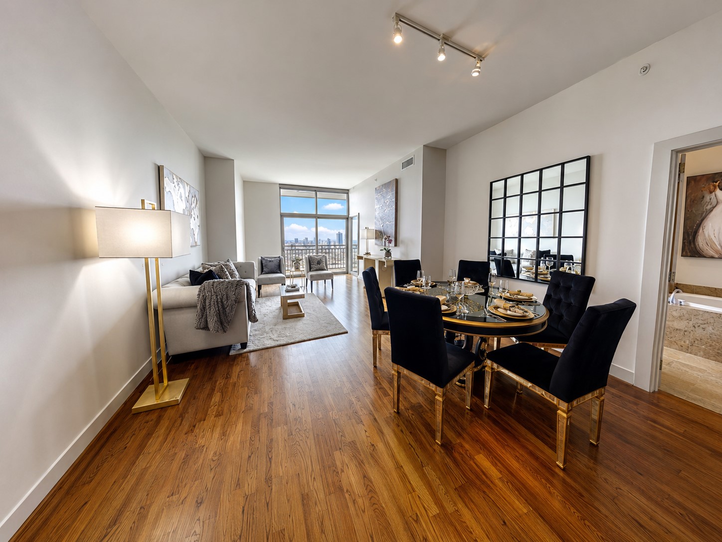 Light-filled living and dining area with warm hardwood floors, sophisticated finishes and expansive windows showcasing elevated city views.