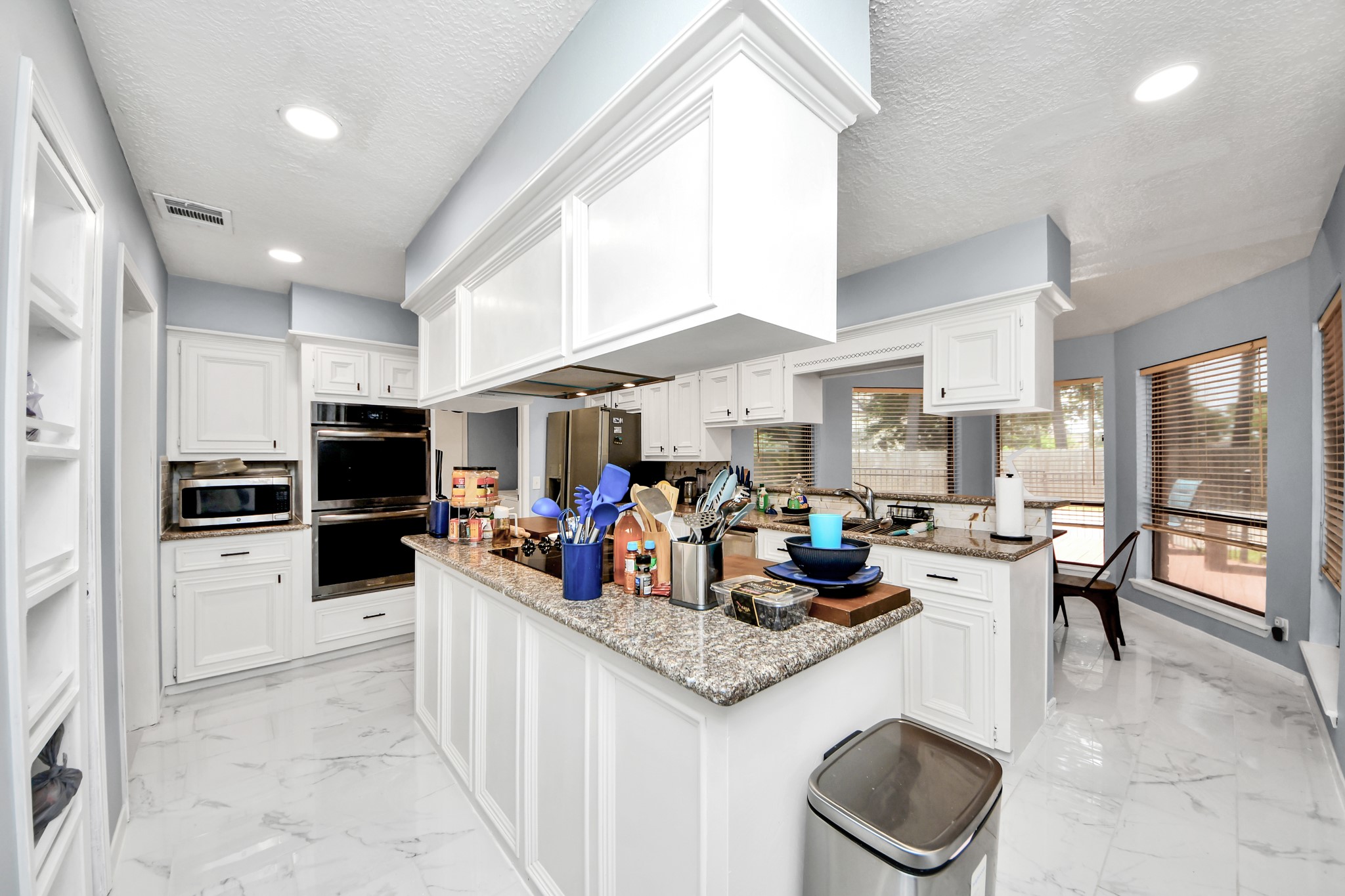 A chefs dream configuration. Bright white cabinetry lines the kitchen to offer abundant storage, centered around an island cooktop and a raised breakfast bar that overlooks the neighboring breakfast area.
