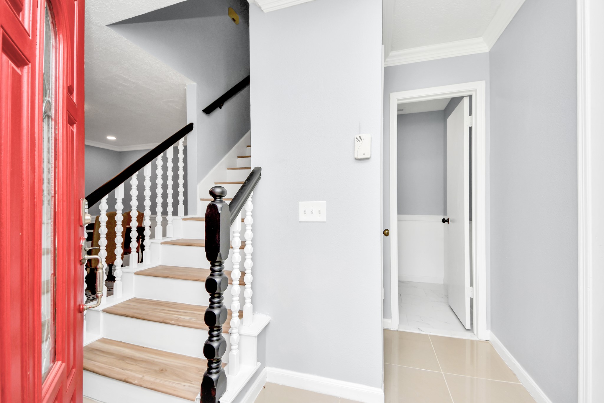 The front door swings open to reveal a stylish, crisp interior where an elegant staircase featuring rich wood treads and contrasting white risers ascends gracefully to the upper level.