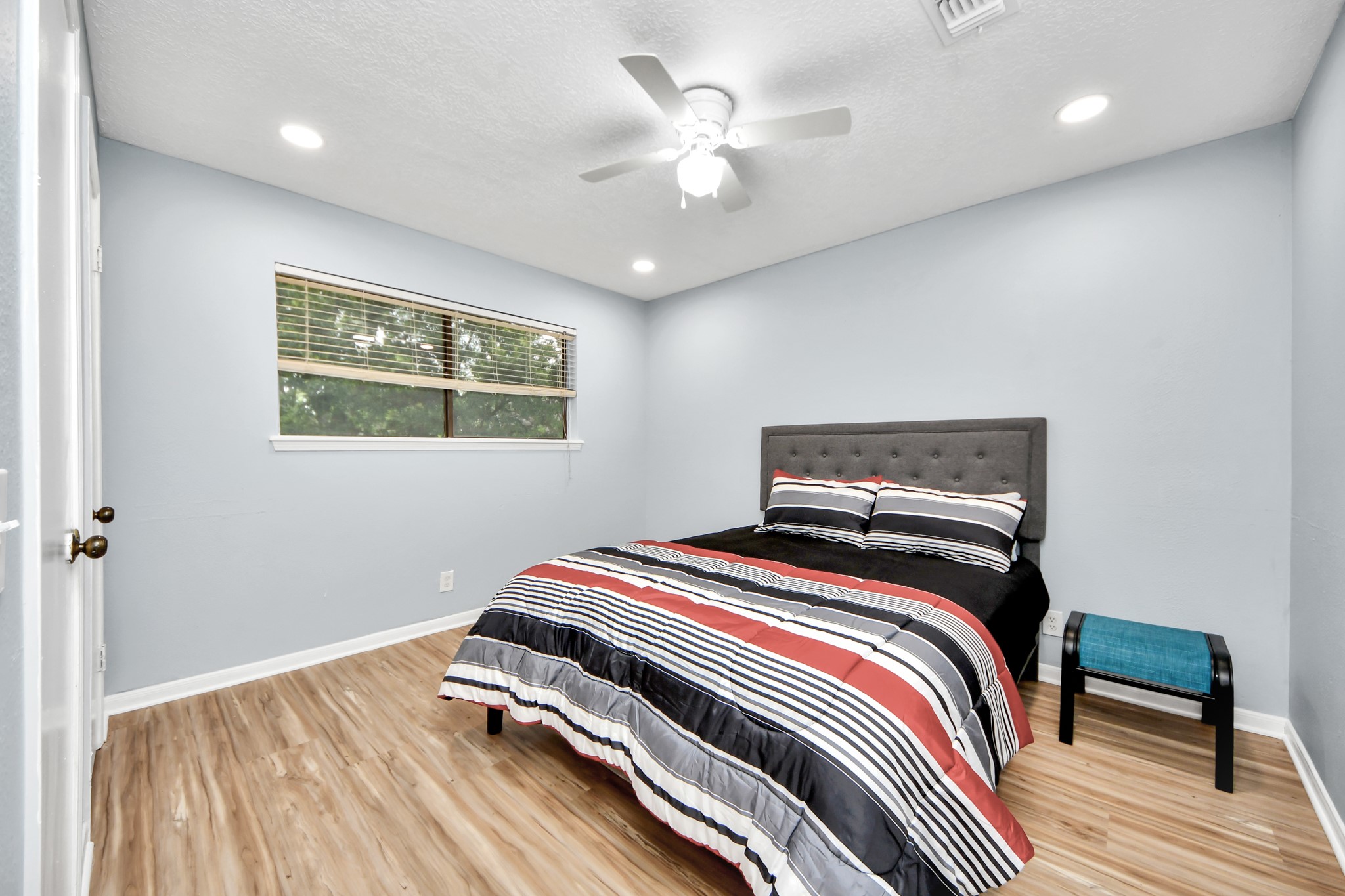 Modern recessed lighting and a ceiling fan elevate this secondary bedroom, which benefits from a wide window.