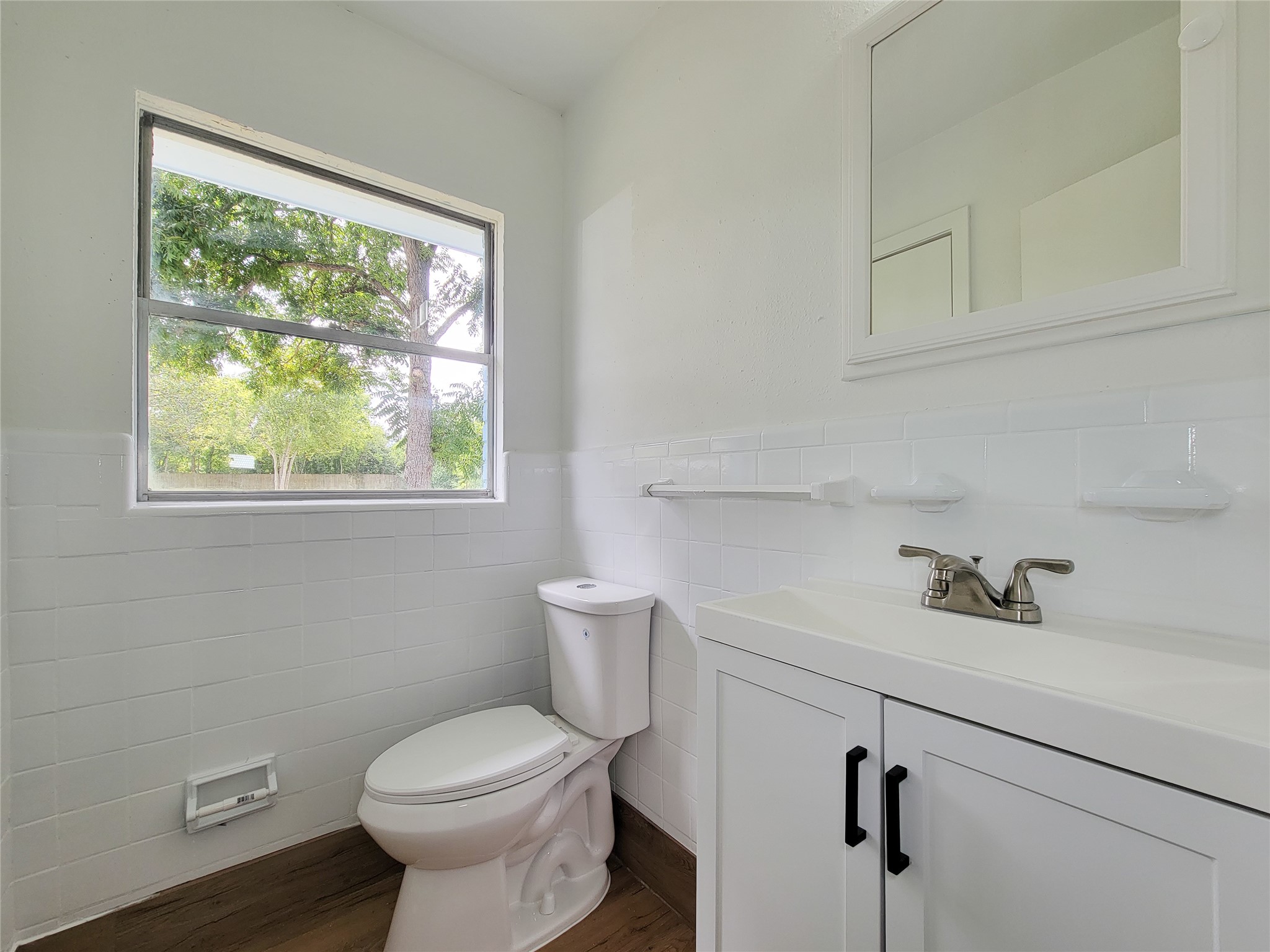 Experience tranquility in this bright and airy bathroom, boasting a large window with serene views, modern white fixtures, and sleek tile accents.