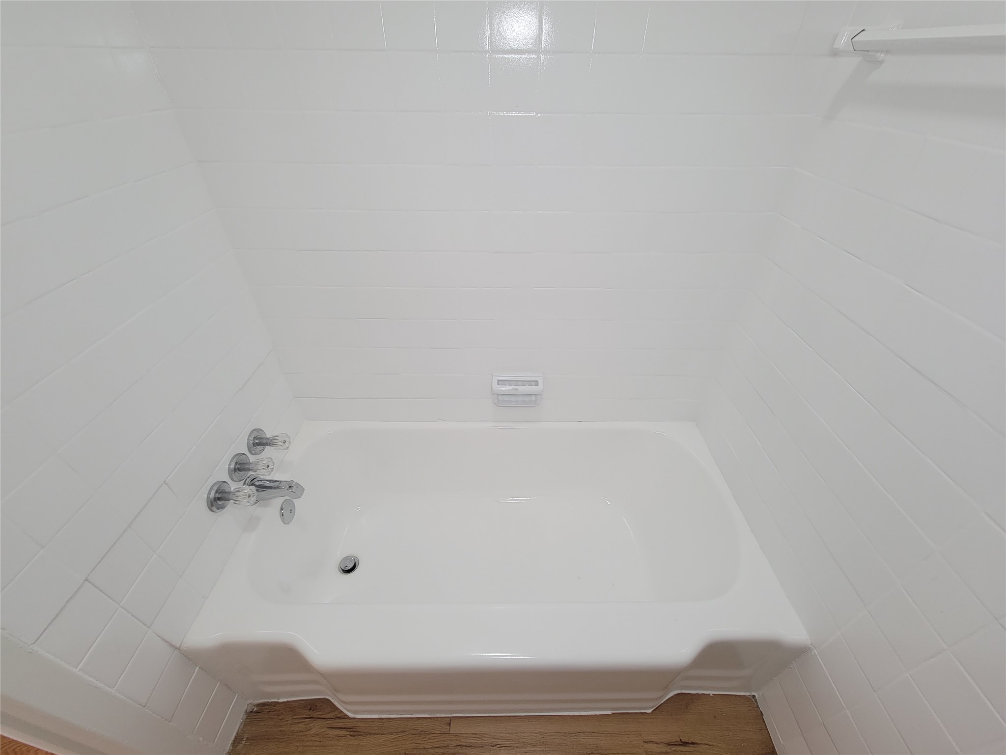 Experience a touch of elegance with this pristine white bathtub, featuring classic chrome fixtures set against sleek, white tile walls.