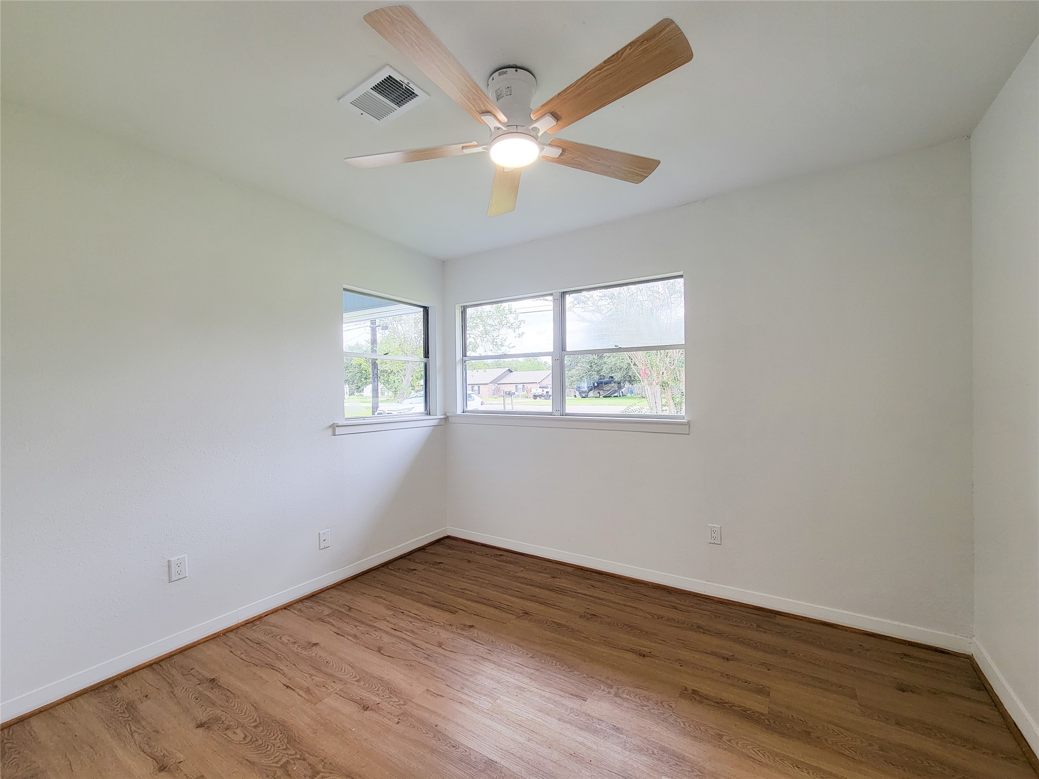 Experience the warmth of this bright and inviting bedroom, featuring large windows, elegant hardwood floors, and a sleek modern ceiling fan.