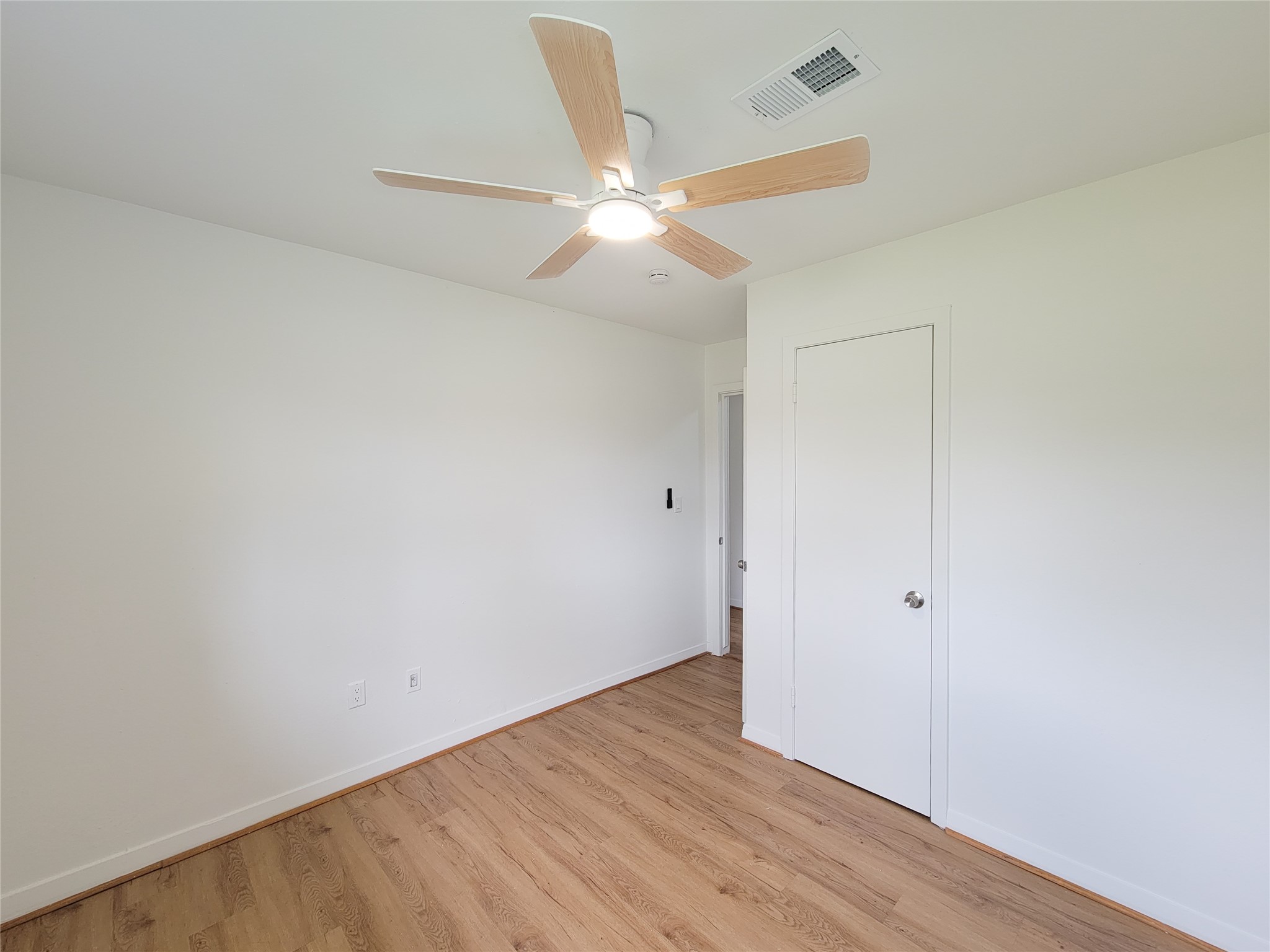Experience the perfect blend of style and comfort in this bright and airy bedroom, featuring fresh white walls, warm wood flooring, and a sleek modern ceiling fan.