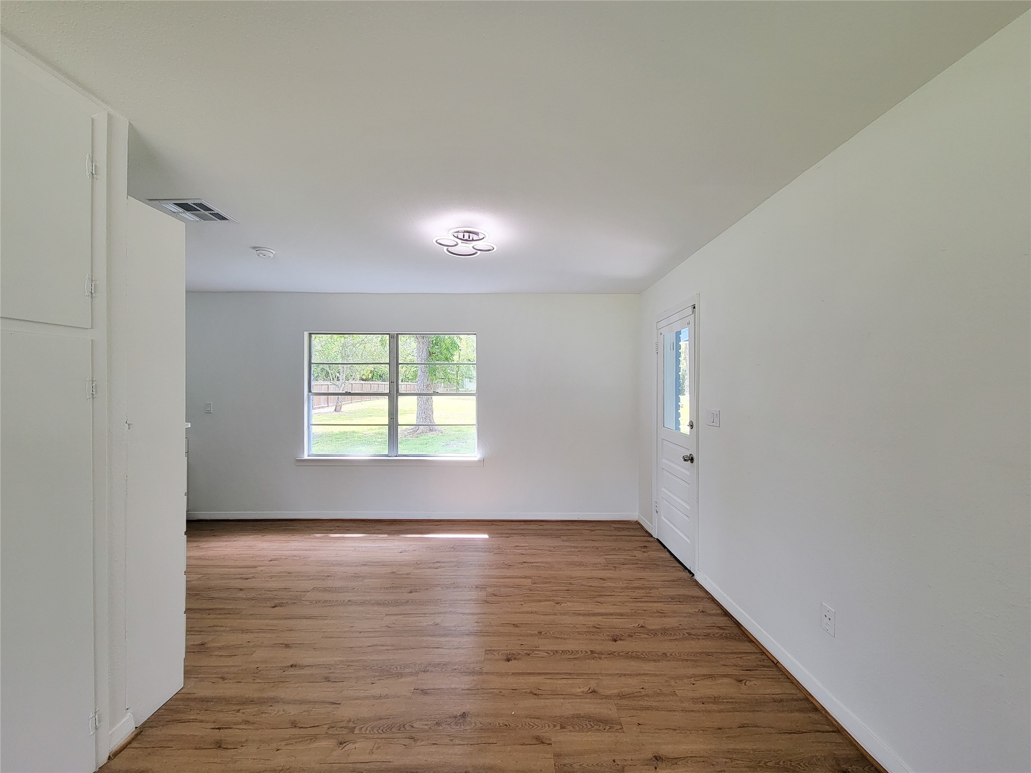 Experience the perfect blend of tranquility and style in this bright living area, featuring fresh white walls, warm wood flooring, and a large window framing serene outdoor views.