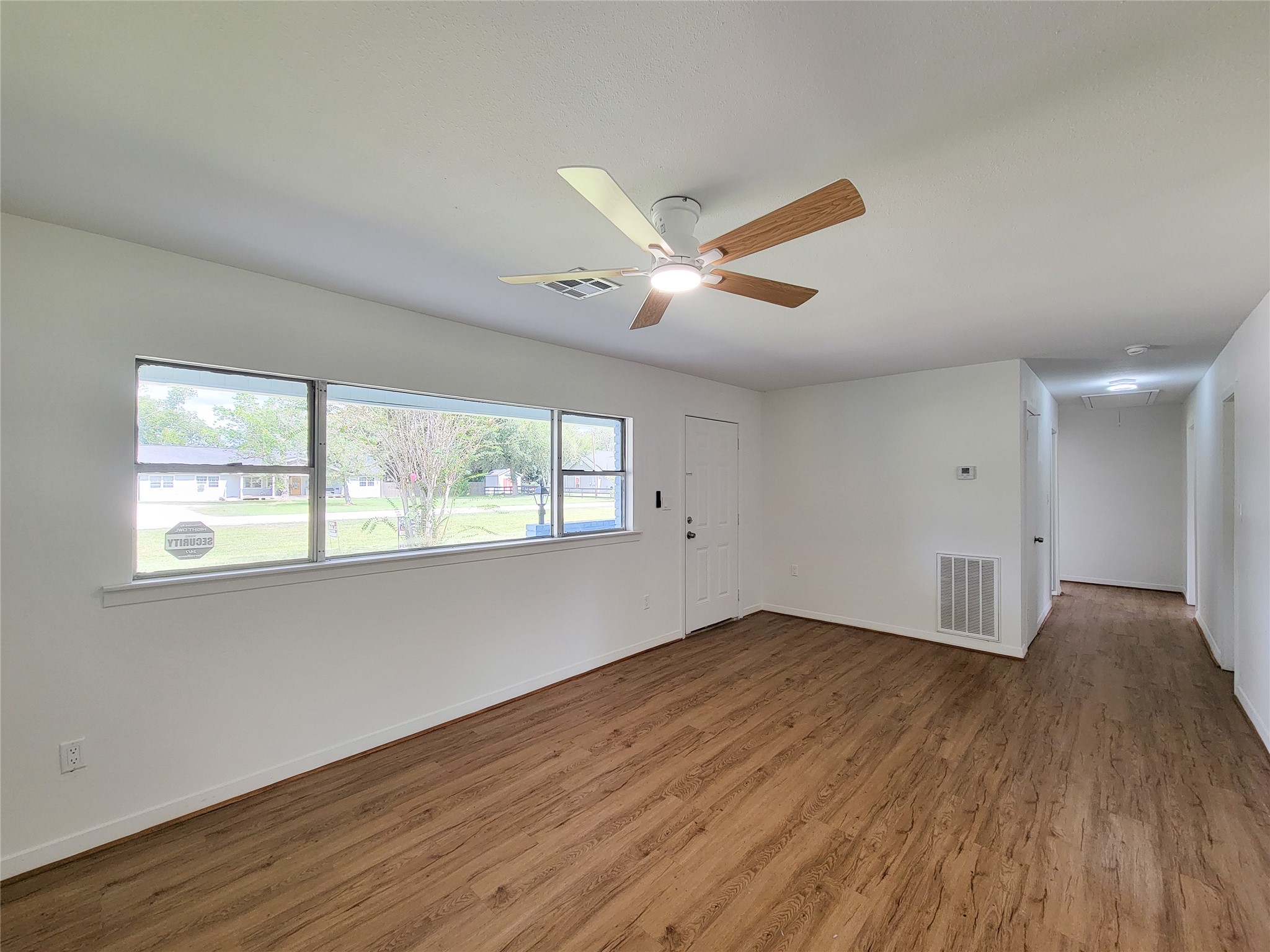 Experience a bright and inviting living space with large windows, sleek wood flooring, and a modern ceiling fan, perfect for creating a welcoming atmosphere. Experience a bright and inviting living space with large windows, sleek wood flooring, and a modern ceiling fan, perfect for creating a welcoming atmosphere.