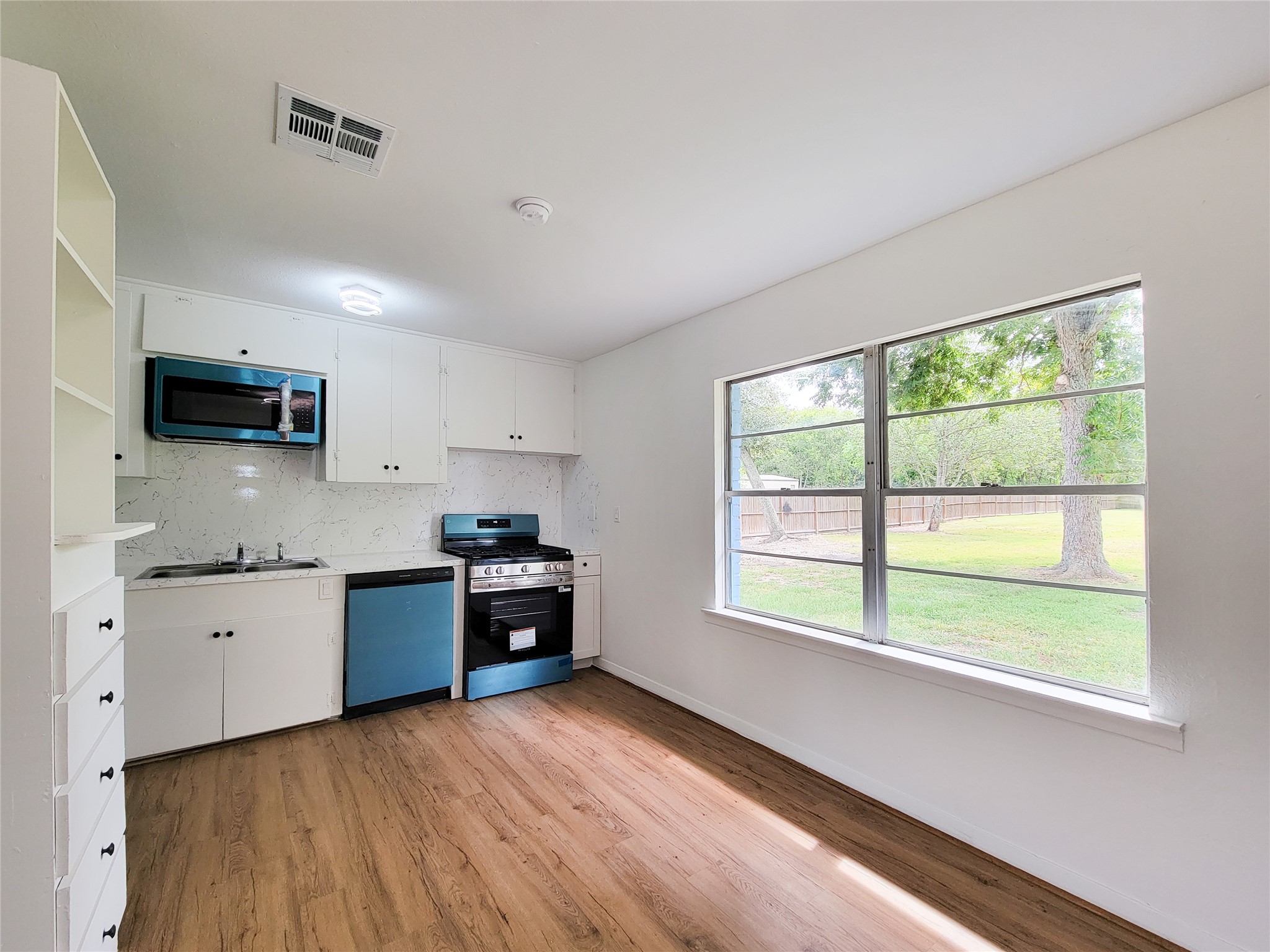 Bright and inviting kitchen featuring modern appliances and sleek white cabinetry, enhanced by large windows with serene views of the expansive backyard.