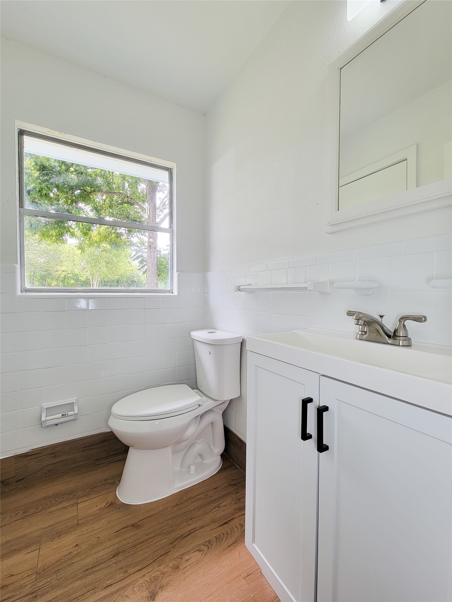 A bright bathroom featuring modern fixtures, a sleek vanity, and elegant wood flooring, all enhanced by a large window that invites natural light.