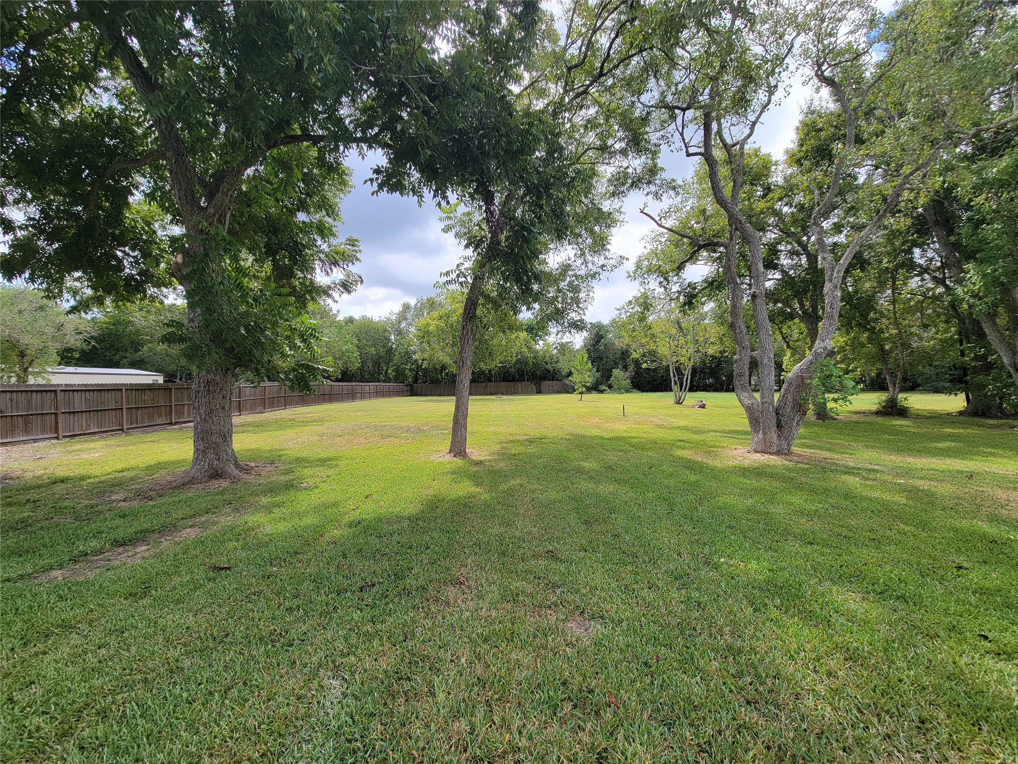 Discover an expansive backyard oasis featuring lush green grass and mature trees, perfect for outdoor activities and relaxation, all within the privacy of a wooden fence.