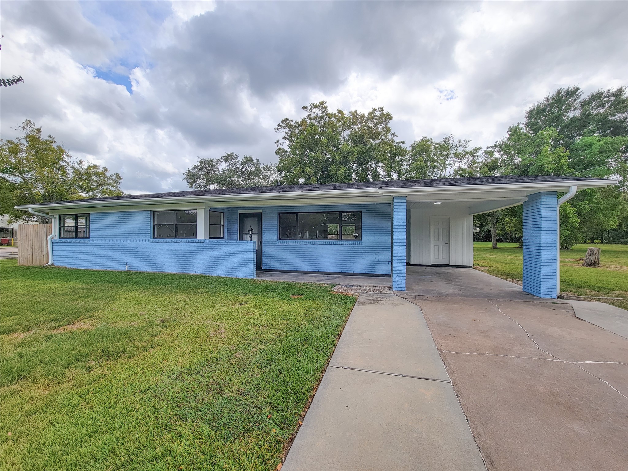 Charming blue ranch-style home with a welcoming front porch and convenient covered carport, all nestled on a spacious, lush green lawn.