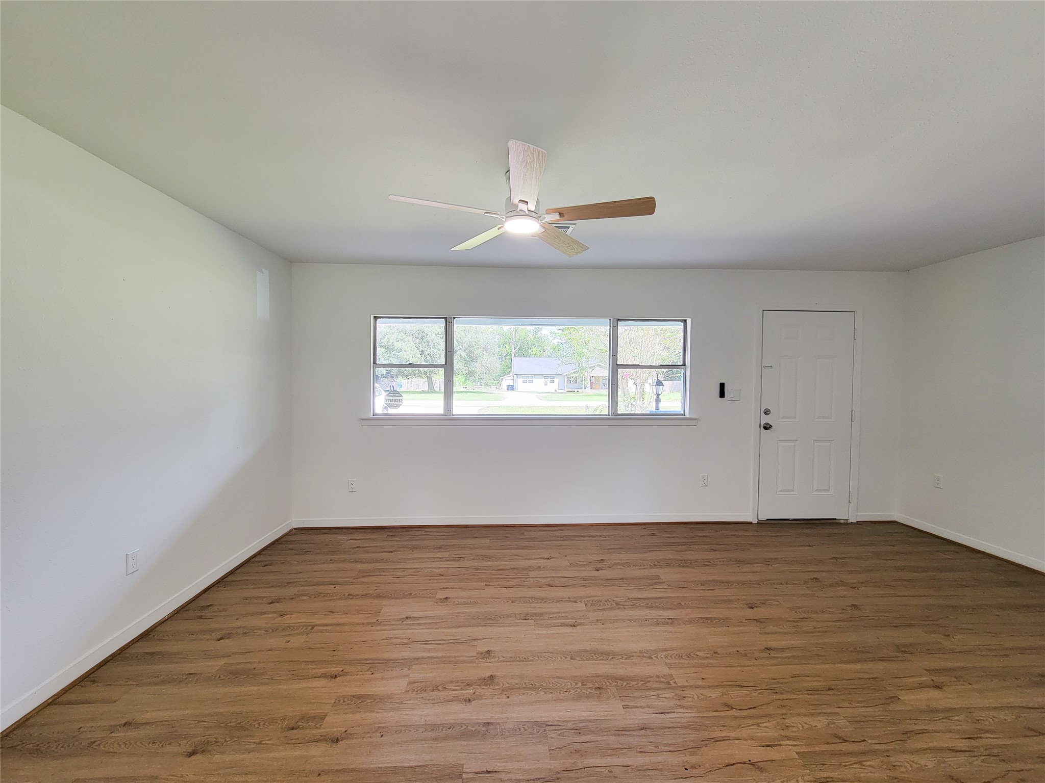 Bright and airy living space with large windows, sleek hardwood flooring, and a modern ceiling fan, creating a welcoming and comfortable ambiance.