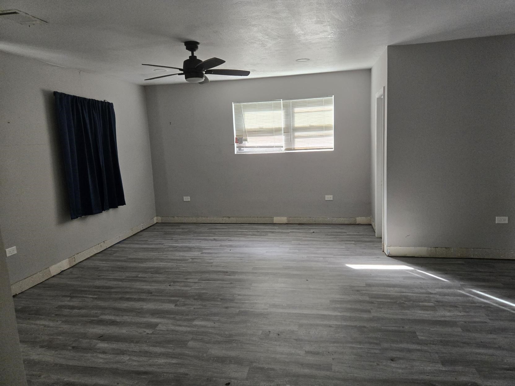 A room with a ceiling fan, a window, and light-colored flooring.