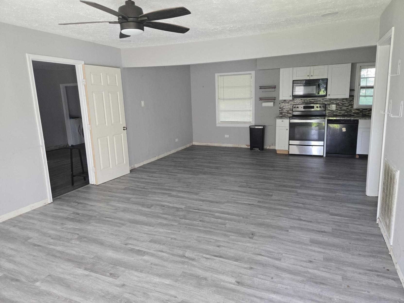 A spacious, modern living area with flooring, and a kitchen featuring stainless steel appliances.