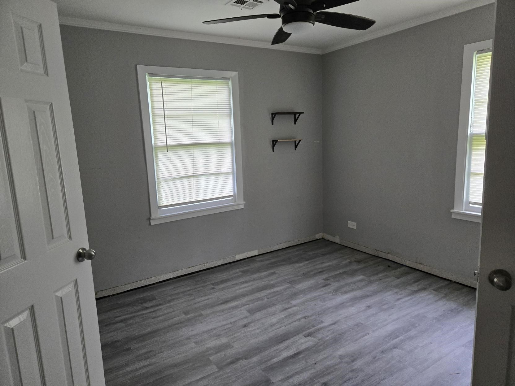 A simple, empty room with a ceiling fan, and wooden floors.