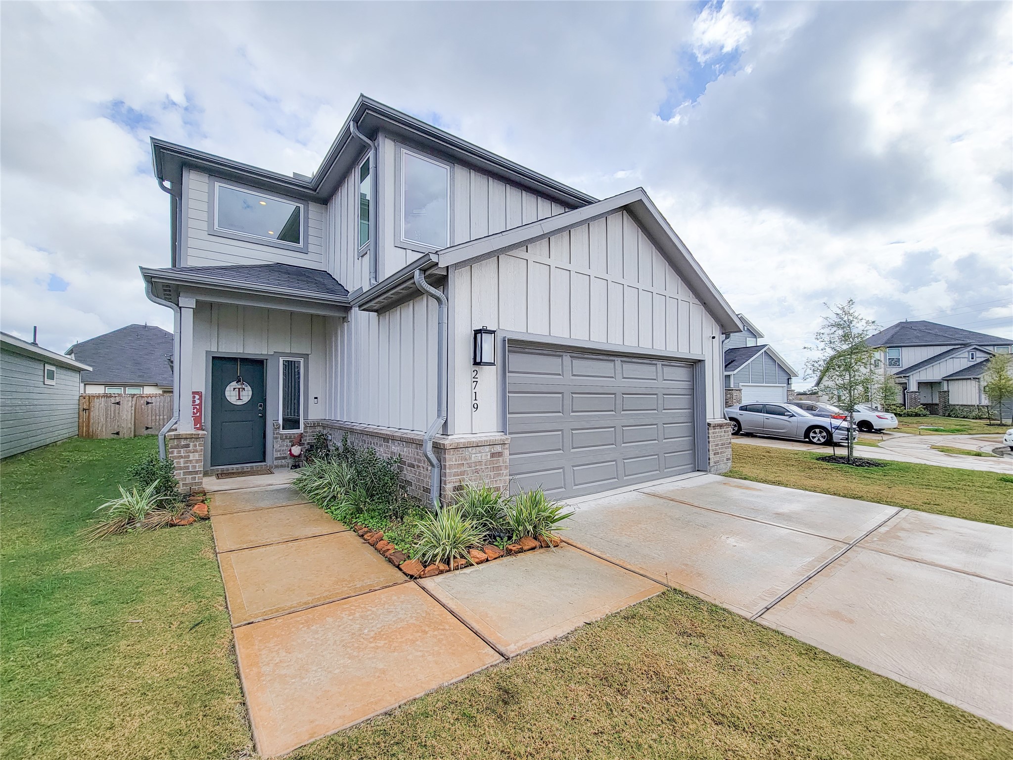 This modern two-story home features a clean gray facade with white trim, a spacious two-car garage, and a well-maintained front yard. The entrance is inviting with a pathway lined with greenery, set in a suburban neighborhood.
