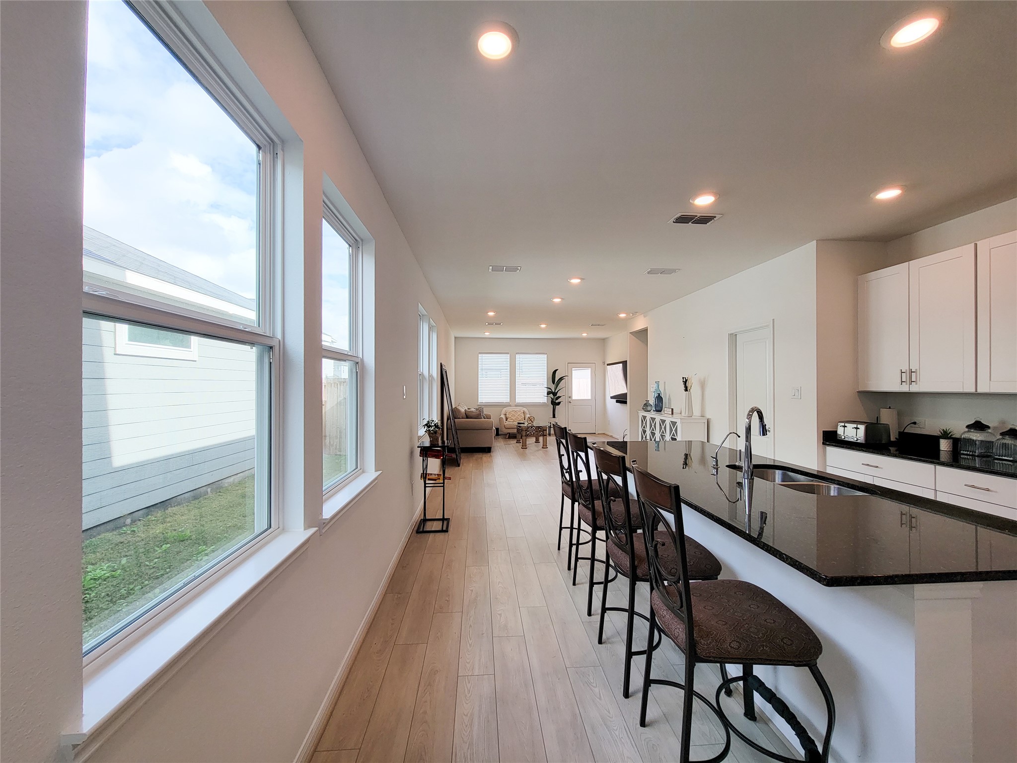 Bright and airy open-plan kitchen and living area with modern finishes. Features a large island with seating, recessed lighting, and ample windows providing natural light.