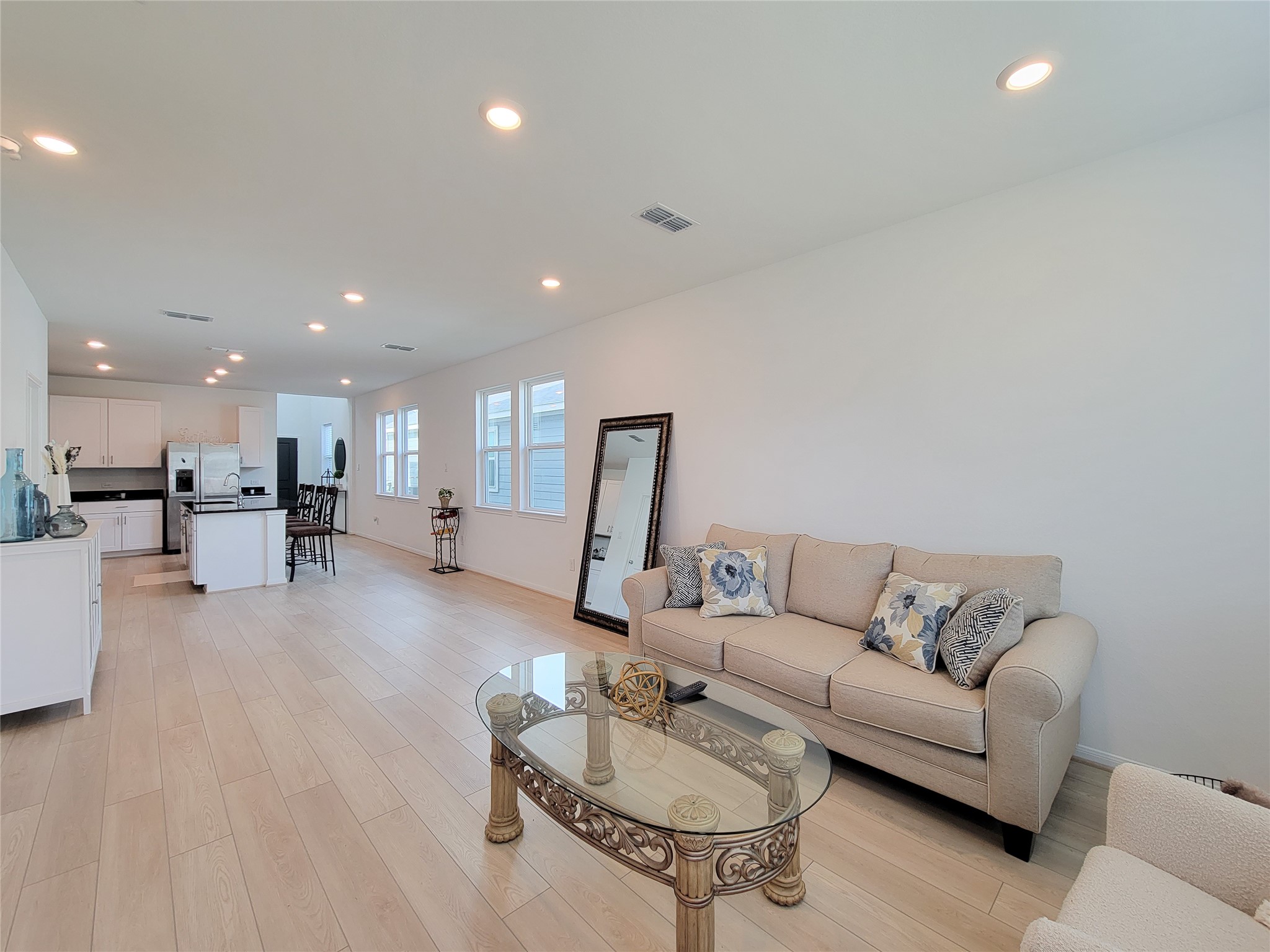 Spacious, open-concept living area with light wood flooring and a modern kitchen. There's ample natural light from large windows.