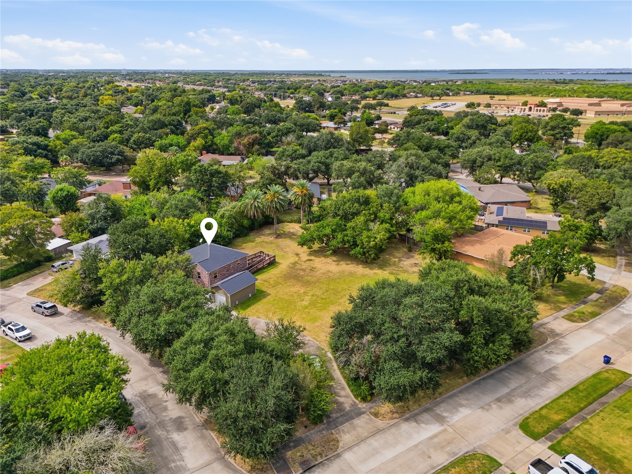 The large corner lot offers open yard space surrounded by mature trees and palms, with a curved driveway leading to the detached garage.