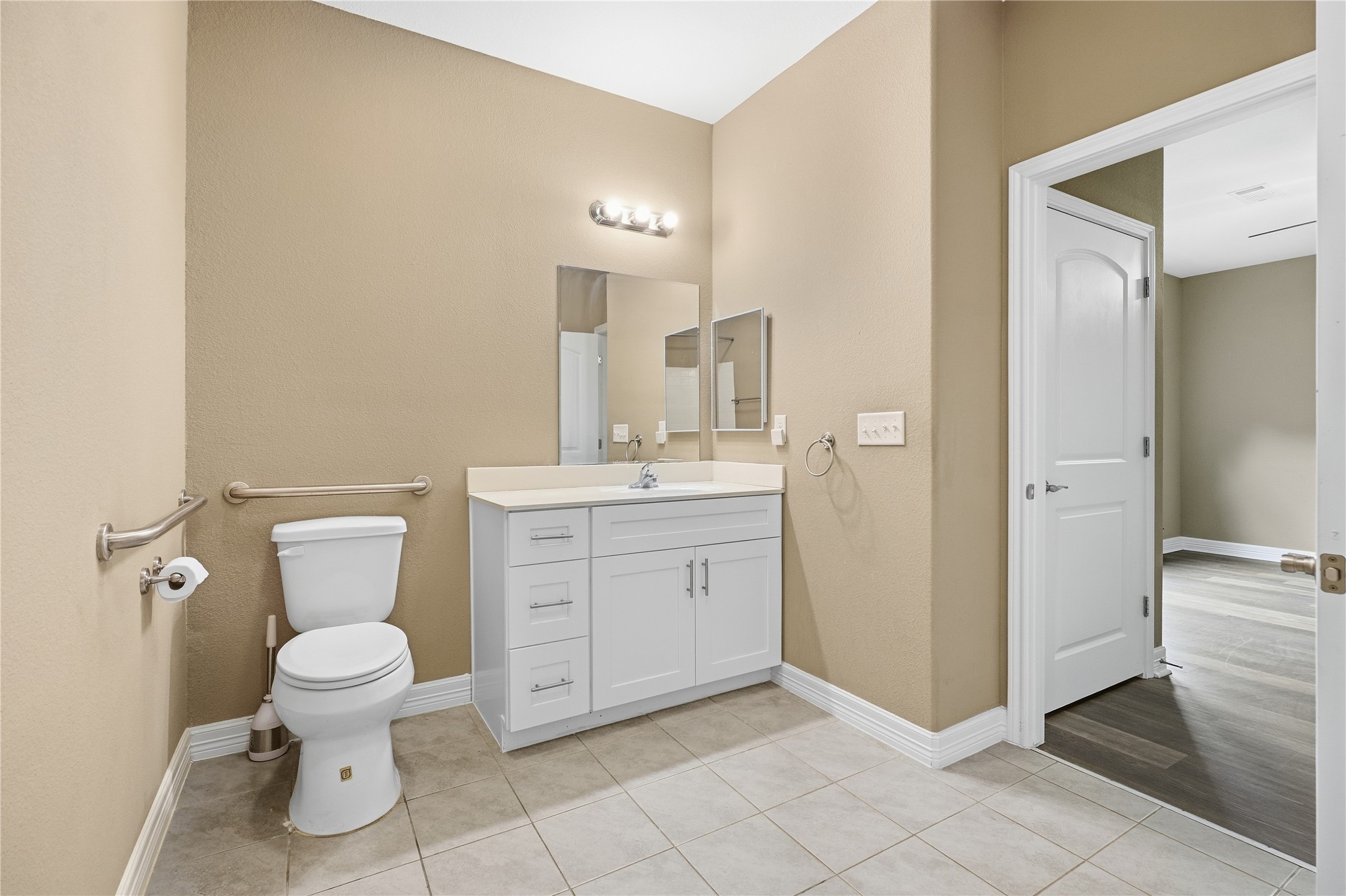 The private primary bathroom features a white vanity with drawer and cabinet storage, plus grab bars beside the toilet.