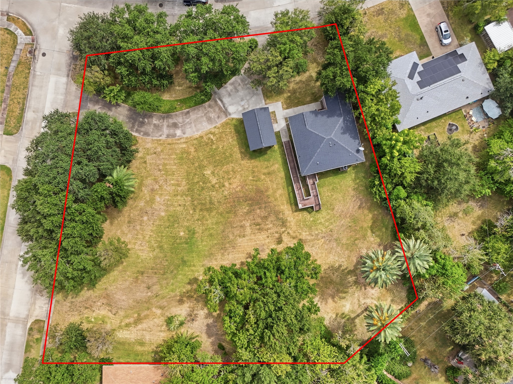 An overhead view highlights the spacious corner lot, with mature trees, open yard space, and a curved driveway leading to the detached garage.