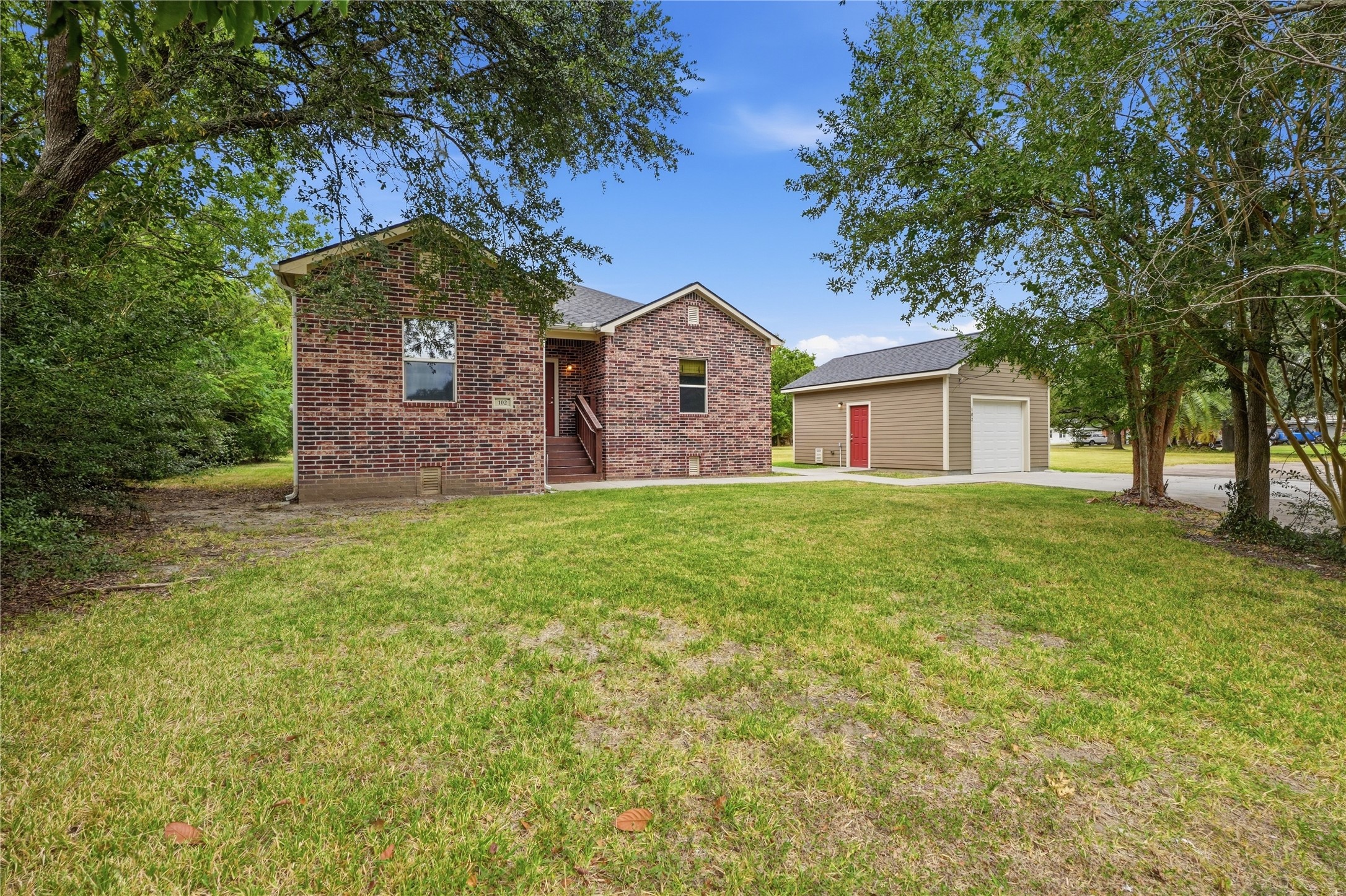 Mature trees frame this brick home, with a spacious front yard, covered entry, and detached garage beside the driveway.