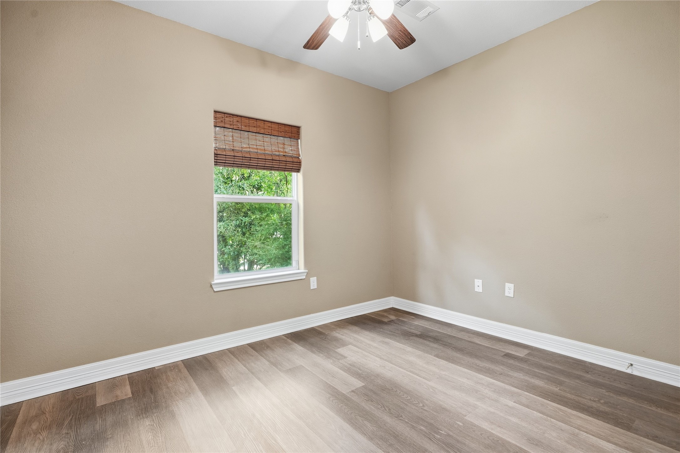 Natural light and a view of the trees brighten this secondary bedroom, featuring neutral colors and a ceiling fan.