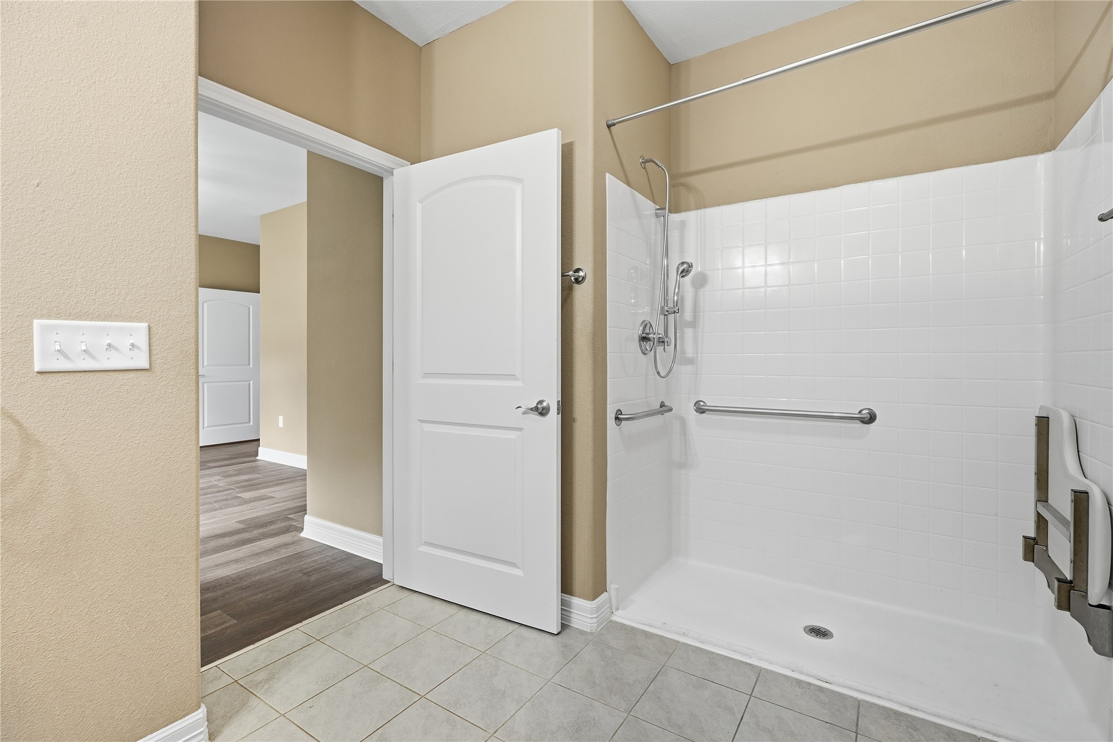 The primary bathroom offers accessibility features including a spacious shower with a handheld showerhead, grab bars, and a fold-down seat.