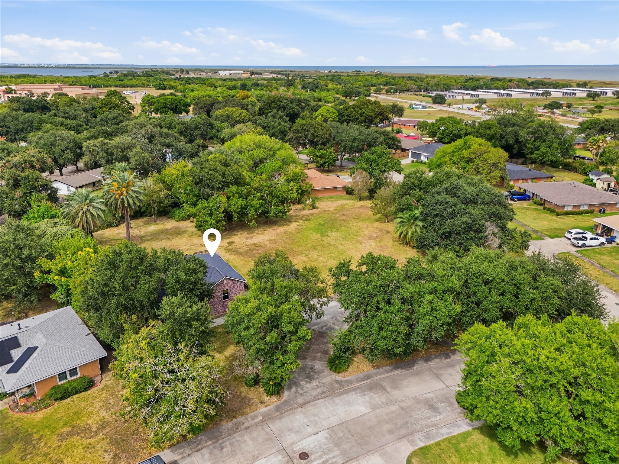 An aerial view of the home and spacious yard, with mature trees and the bay visible in the distance.