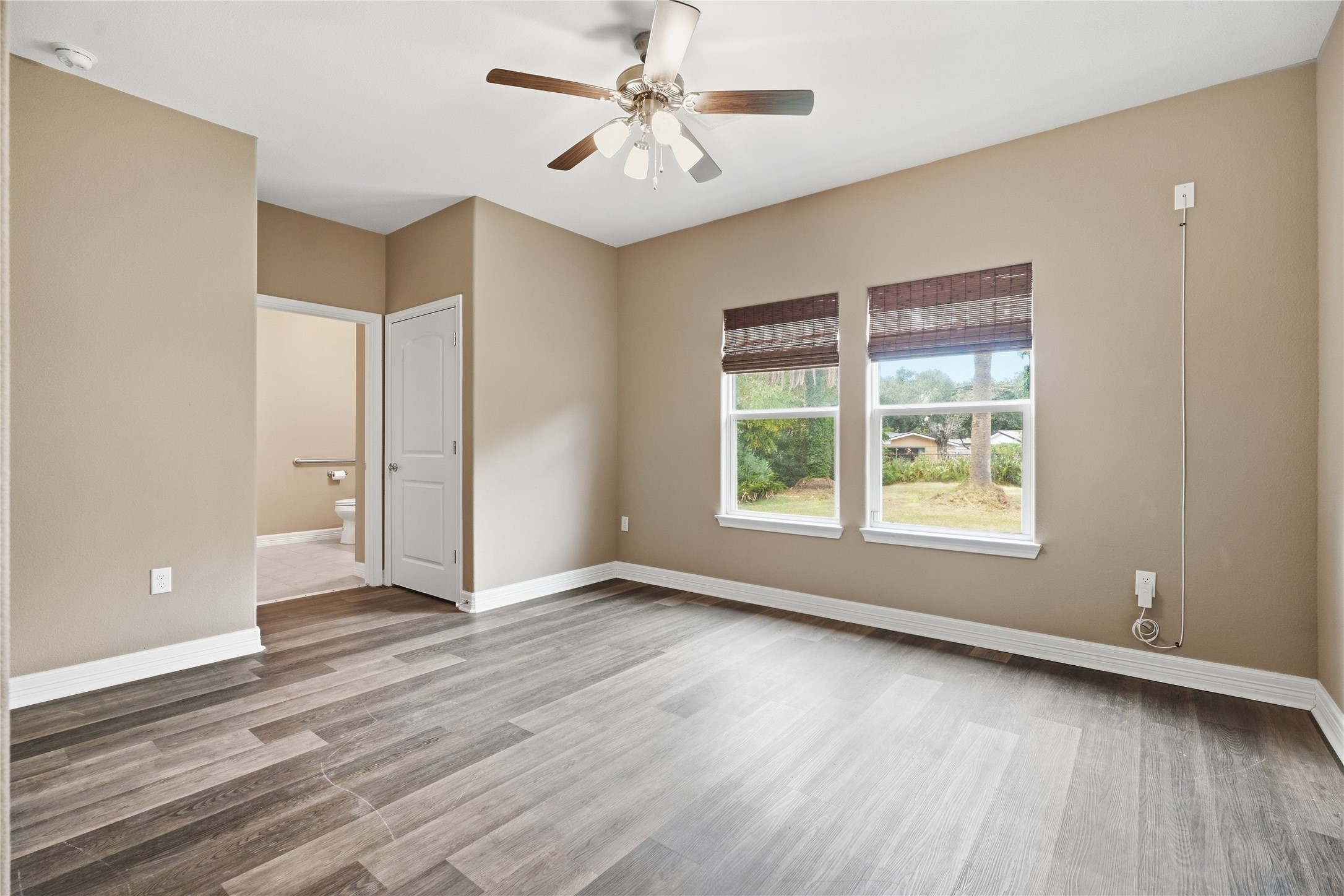 Two windows overlooking the backyard bring natural light into the primary bedroom, which features a ceiling fan and a private bathroom.