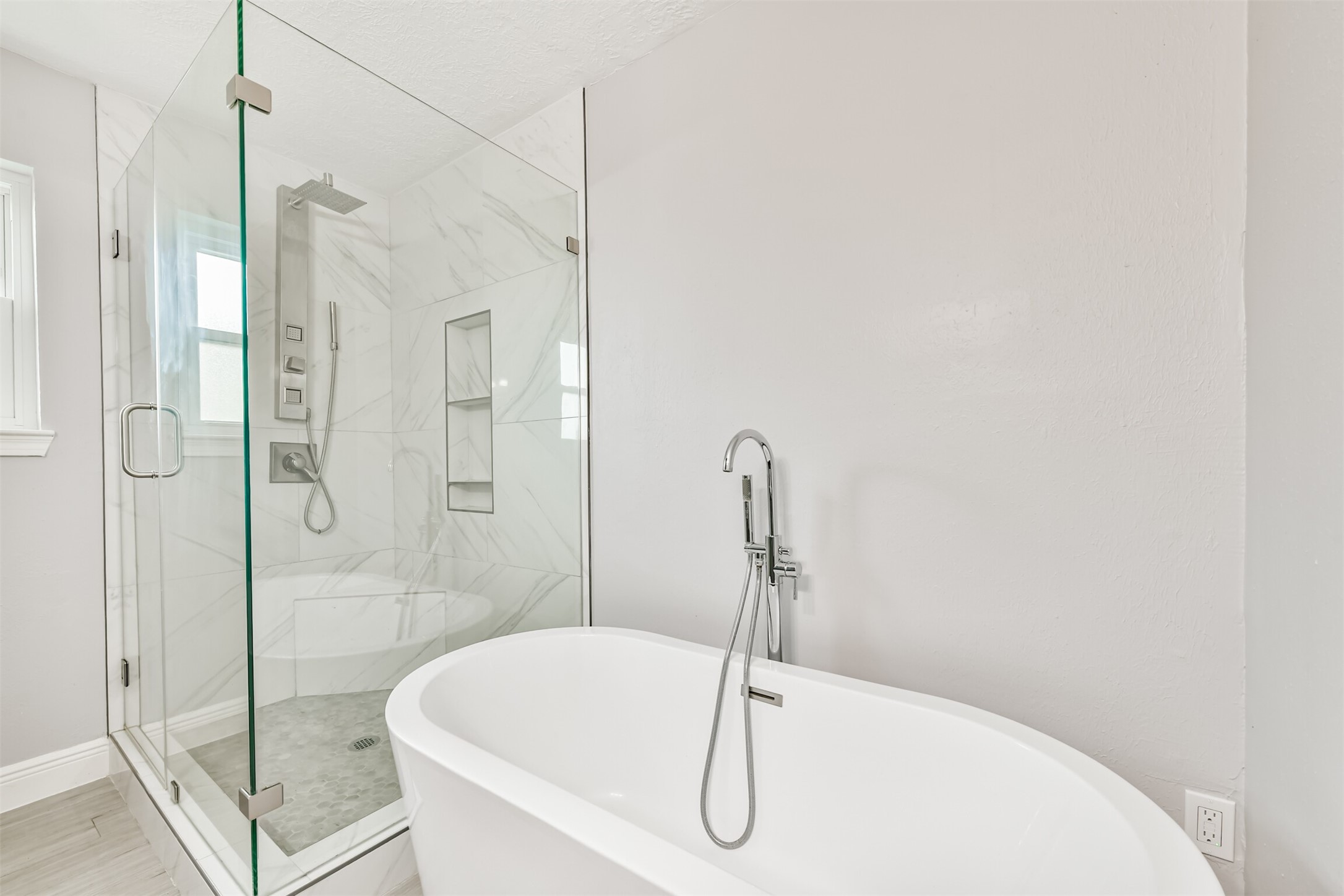 Experience luxury in this primary bath, featuring a modern freestanding tub and a sleek glass-enclosed shower with elegant tilework.