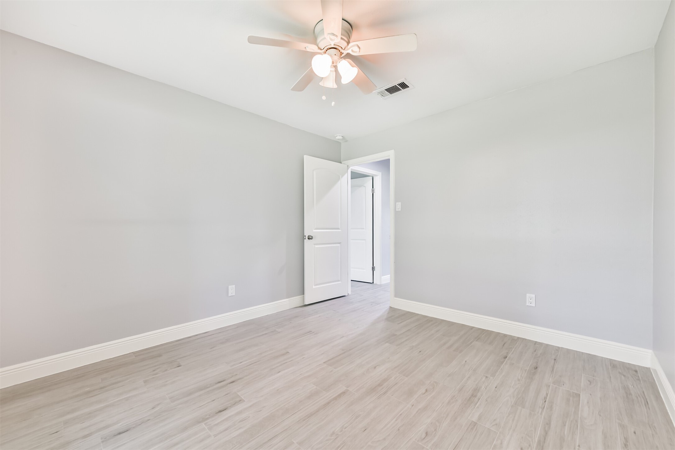 Bright and inviting, this spacious bedroom features sleek flooring and a modern ceiling fan, perfect for comfort and style.