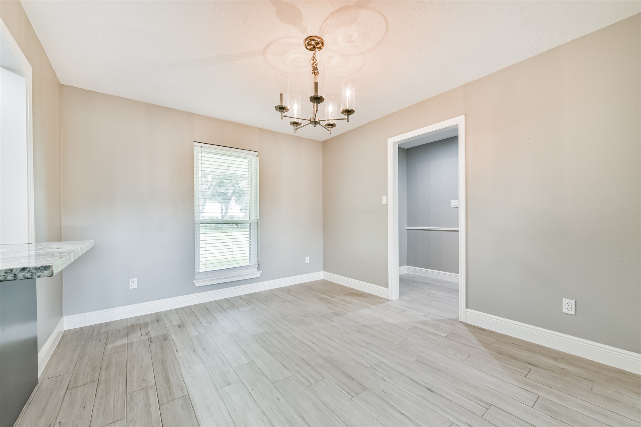 Bright and inviting breakfast nook featuring elegant wood flooring, a stylish chandelier, and a large window for natural light. Perfect for morning coffee and casual dining.