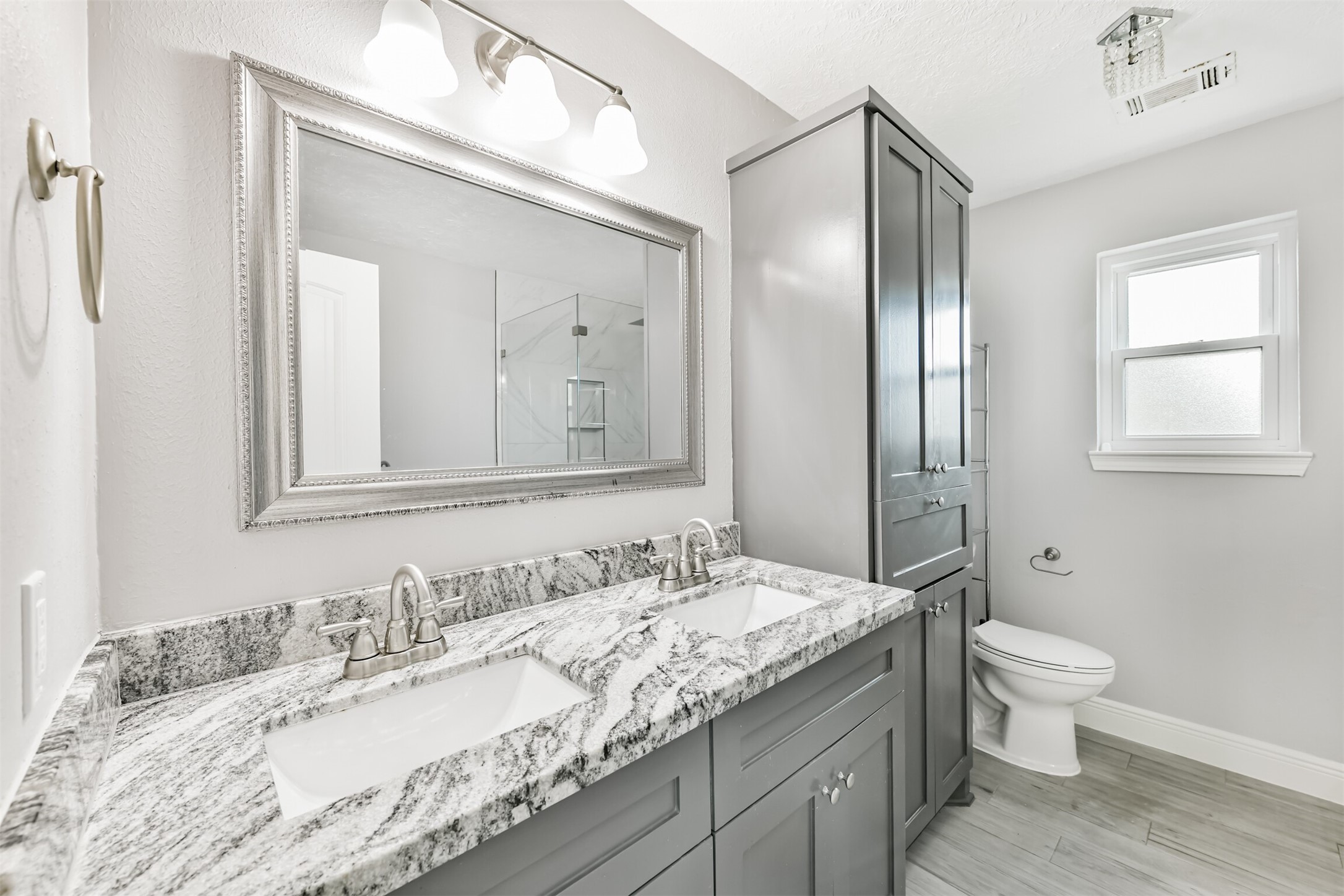 Experience luxury in the primary bath featuring dual sinks with elegant granite countertops, modern fixtures, and ample storage, all bathed in natural light.