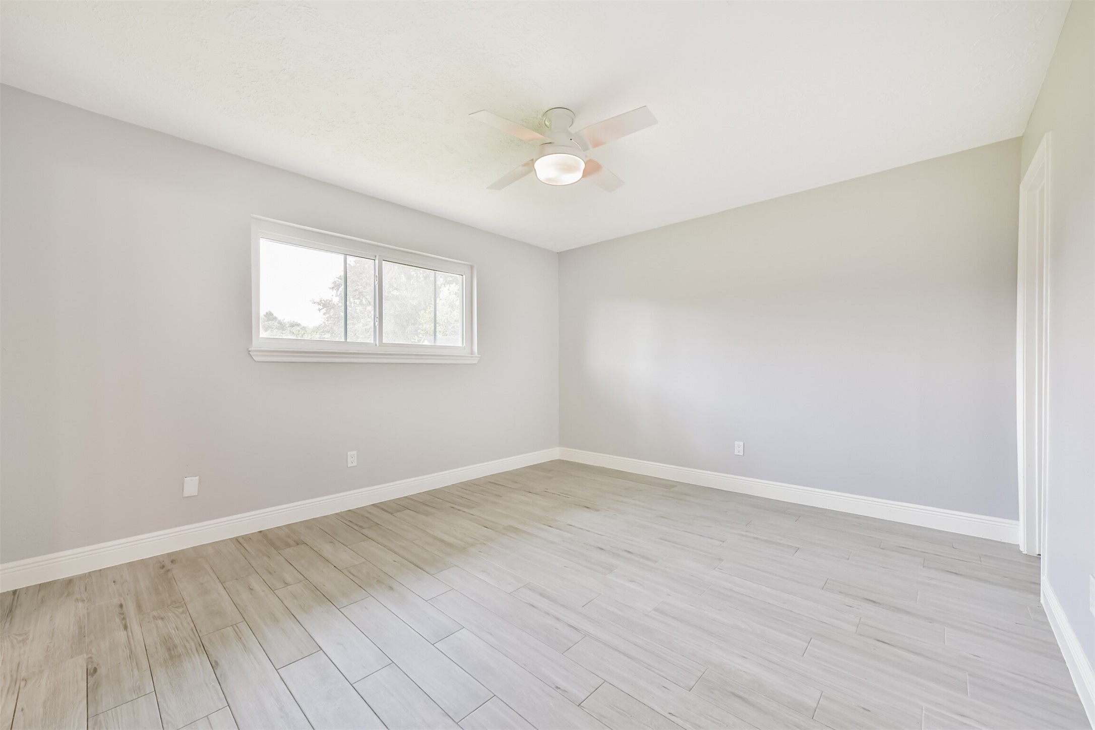Spacious primary bedroom featuring sleek flooring, abundant natural light, and a stylish ceiling fan.
