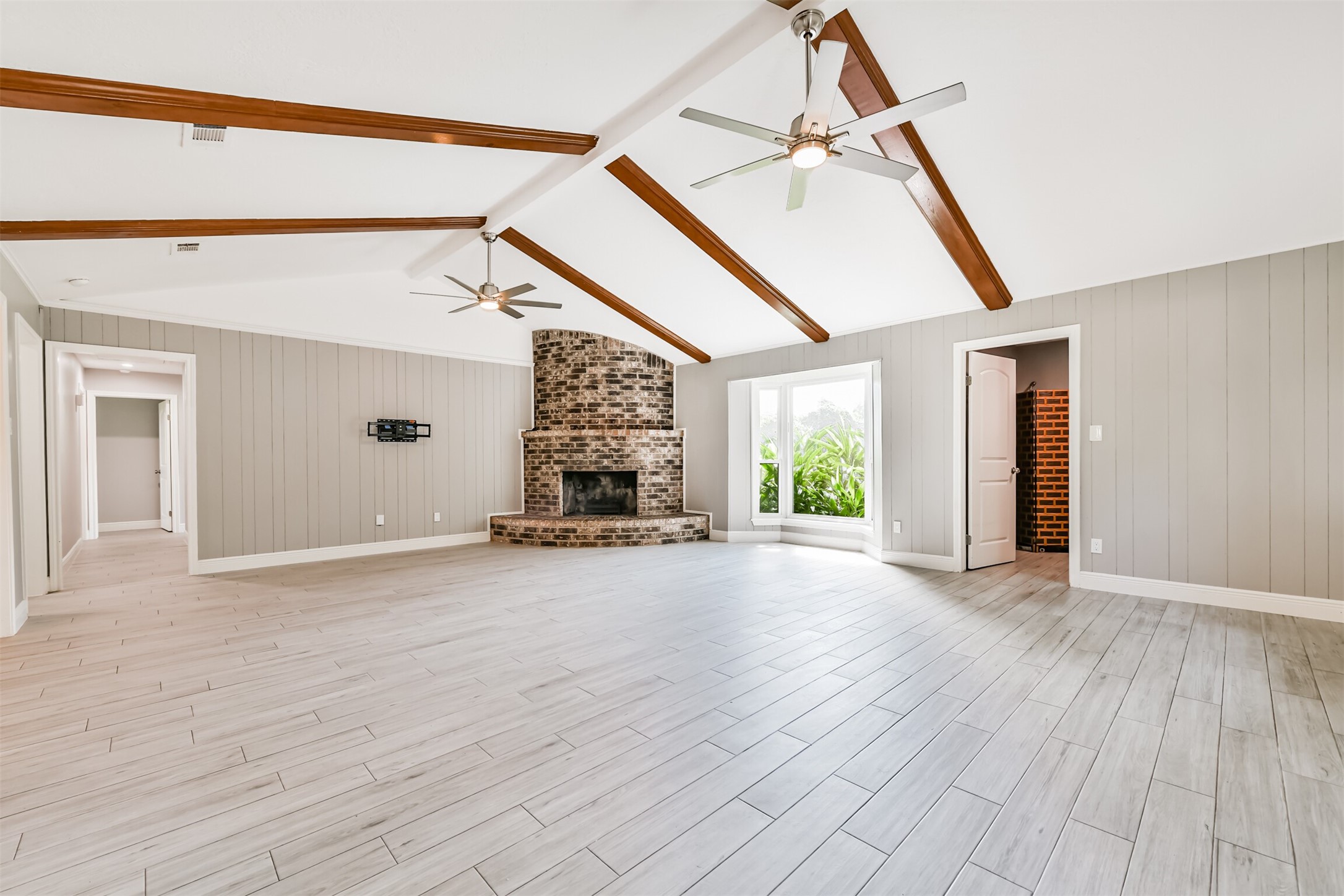 Spacious and inviting living area featuring high ceilings with elegant wood beams, a charming brick fireplace, and abundant natural light. Perfect for entertaining and relaxing.