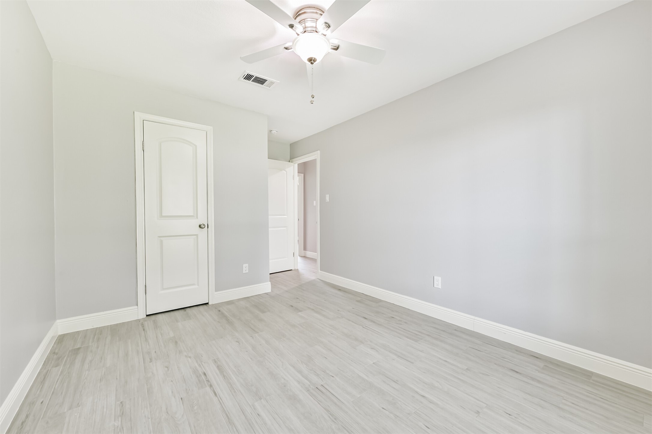 Here is a bright and inviting bedroom, featuring fresh neutral tones, sleek flooring, and a modern ceiling fan, perfect for a cozy retreat.
