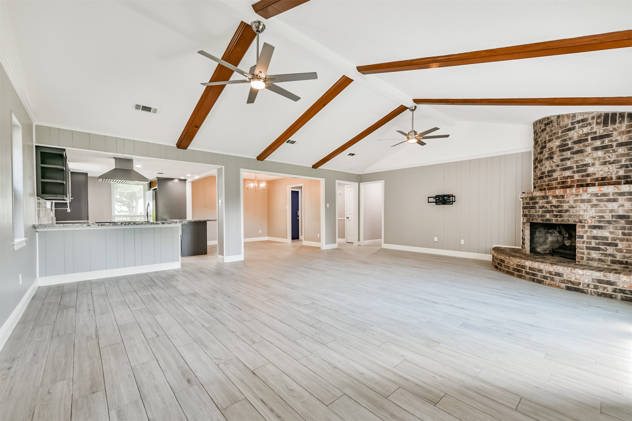 Spacious and inviting living area featuring vaulted ceilings, elegant wood beams, and a striking brick fireplace. Perfect for modern living and entertaining.