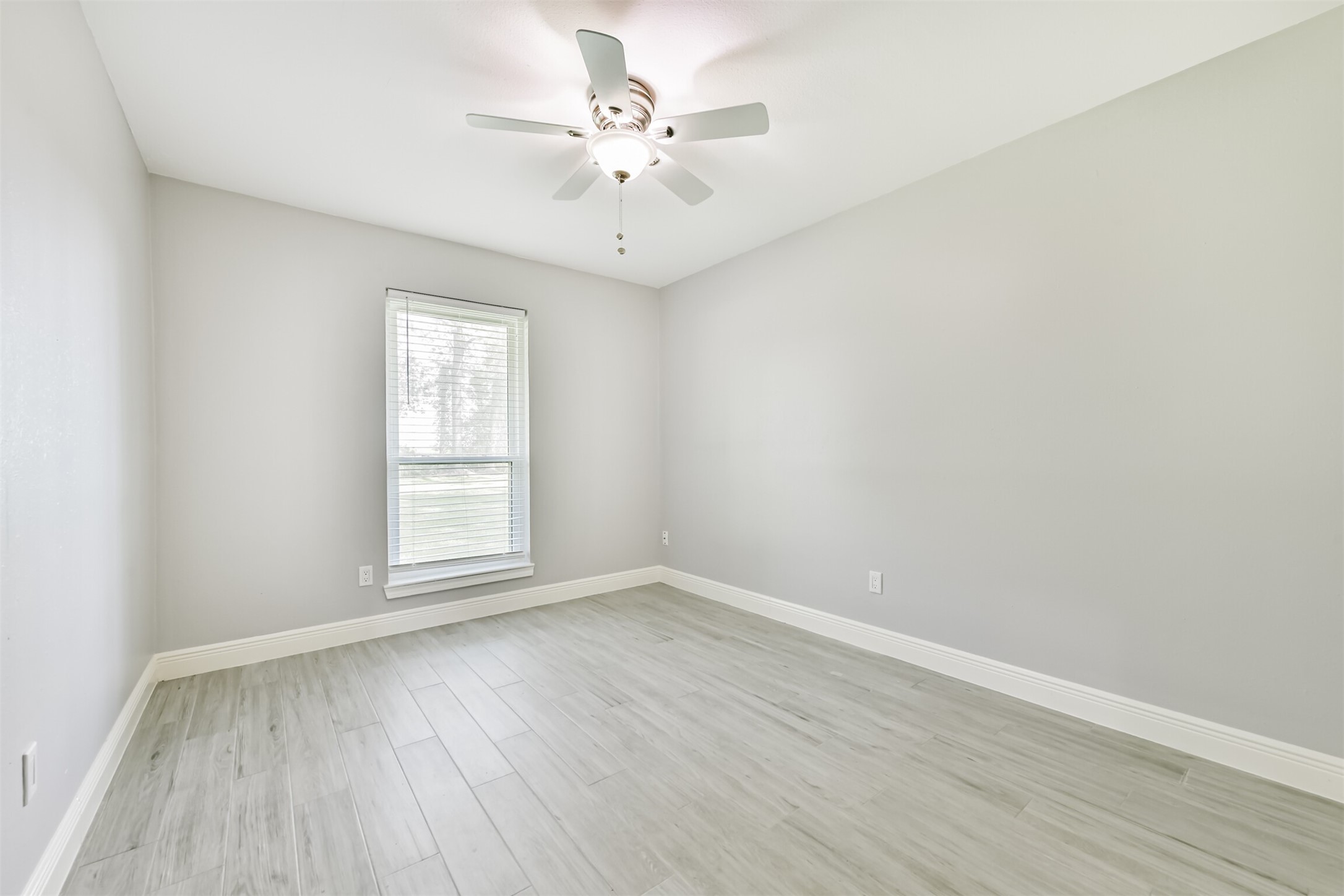 Spacious and bright bedroom featuring elegant wood flooring and a large window for natural light.