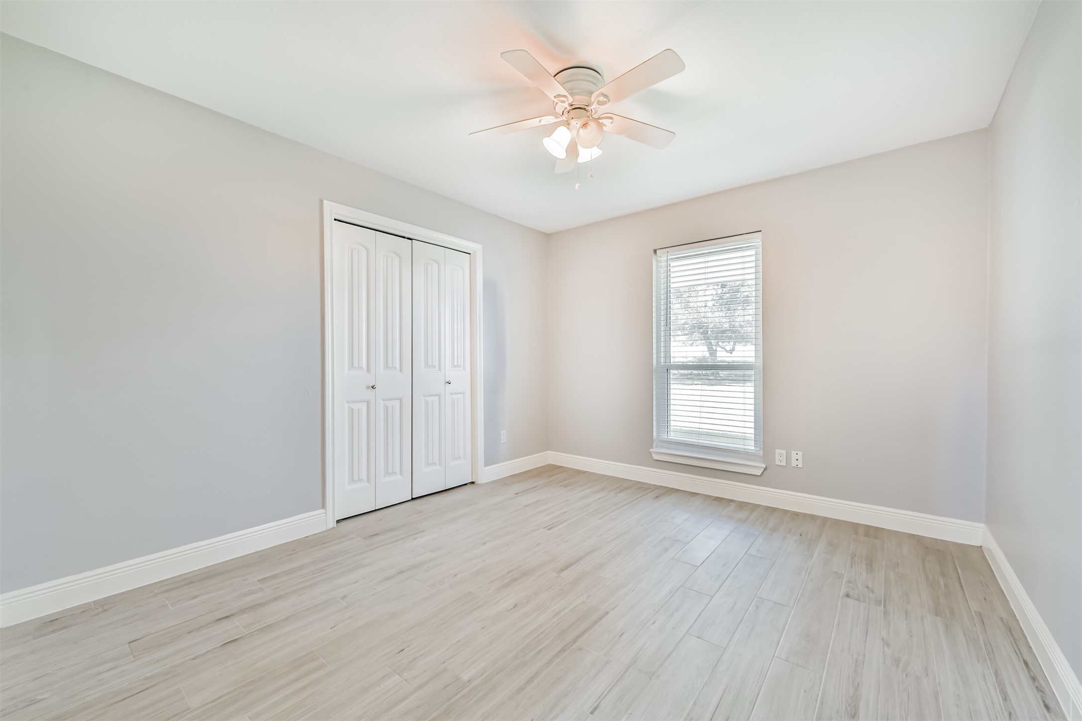 Bright and airy second bedroom featuring sleek flooring, a ceiling fan, and a spacious closet, perfect for comfort and functionality.