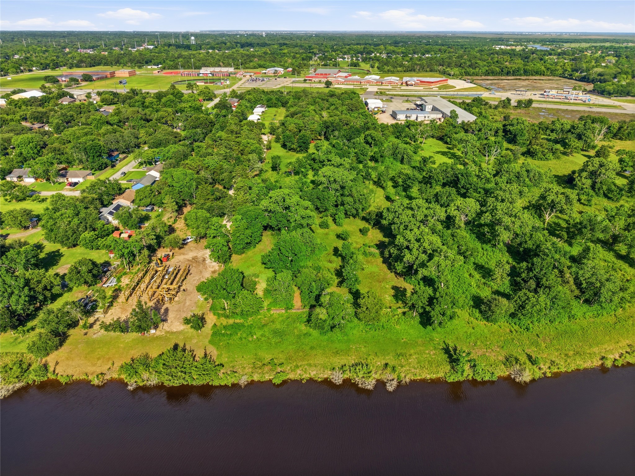 Expansive aerial view of a lush, green property with dense trees, adjacent to a serene river.