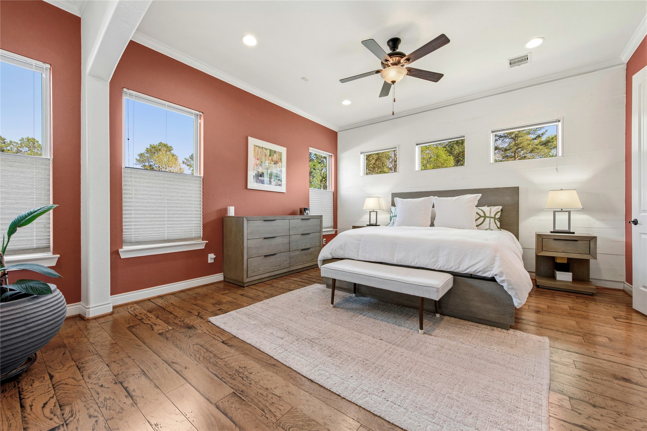 Primary bedroom with spacious floor plan, hardwood floors and warm accent walls.