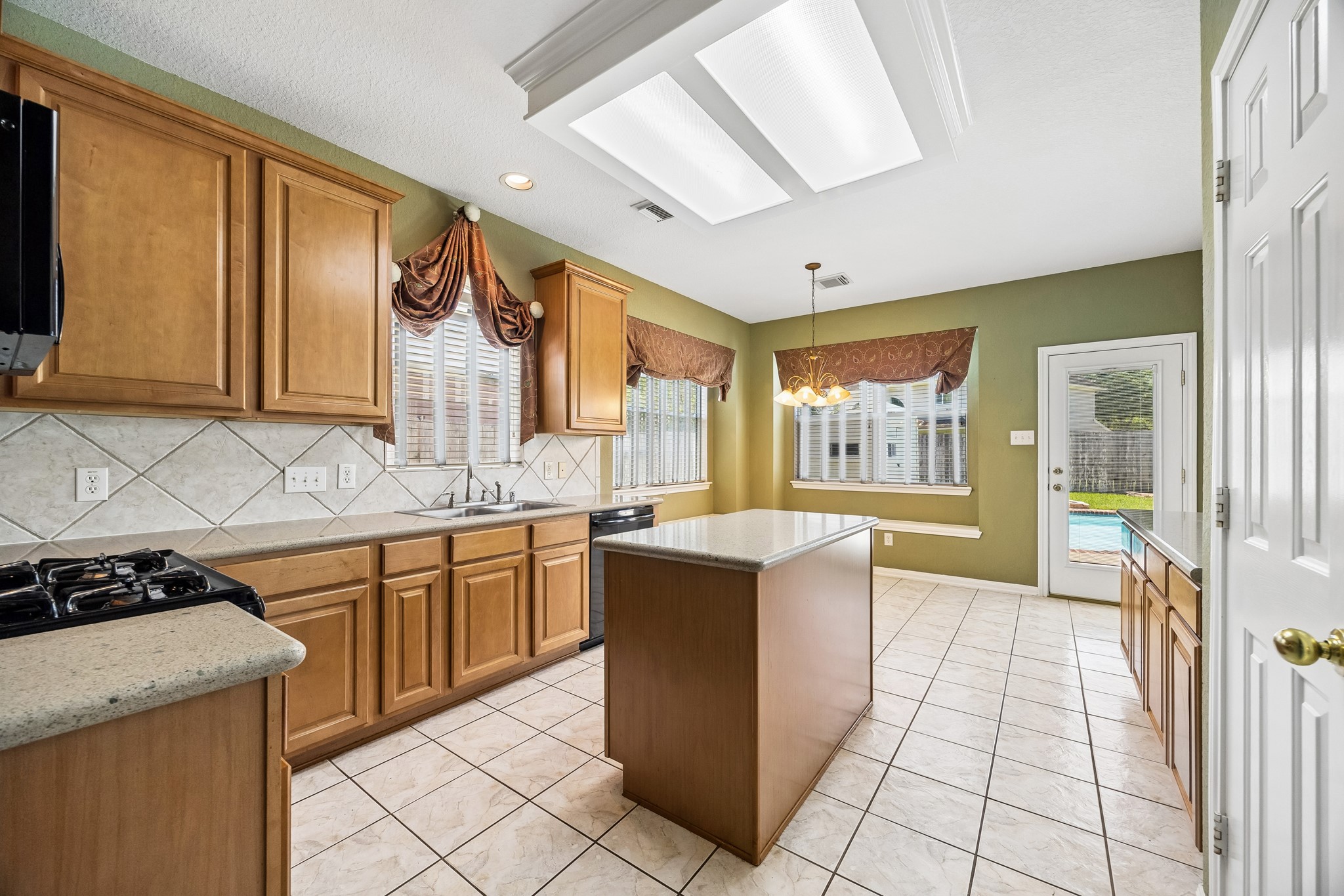 This spotless kitchen is ready for busy mornings and weeknight dinners with quartz counters, classic wood cabinetry, tile backsplash, sleek black appliances and plenty of prep space with a large center island.