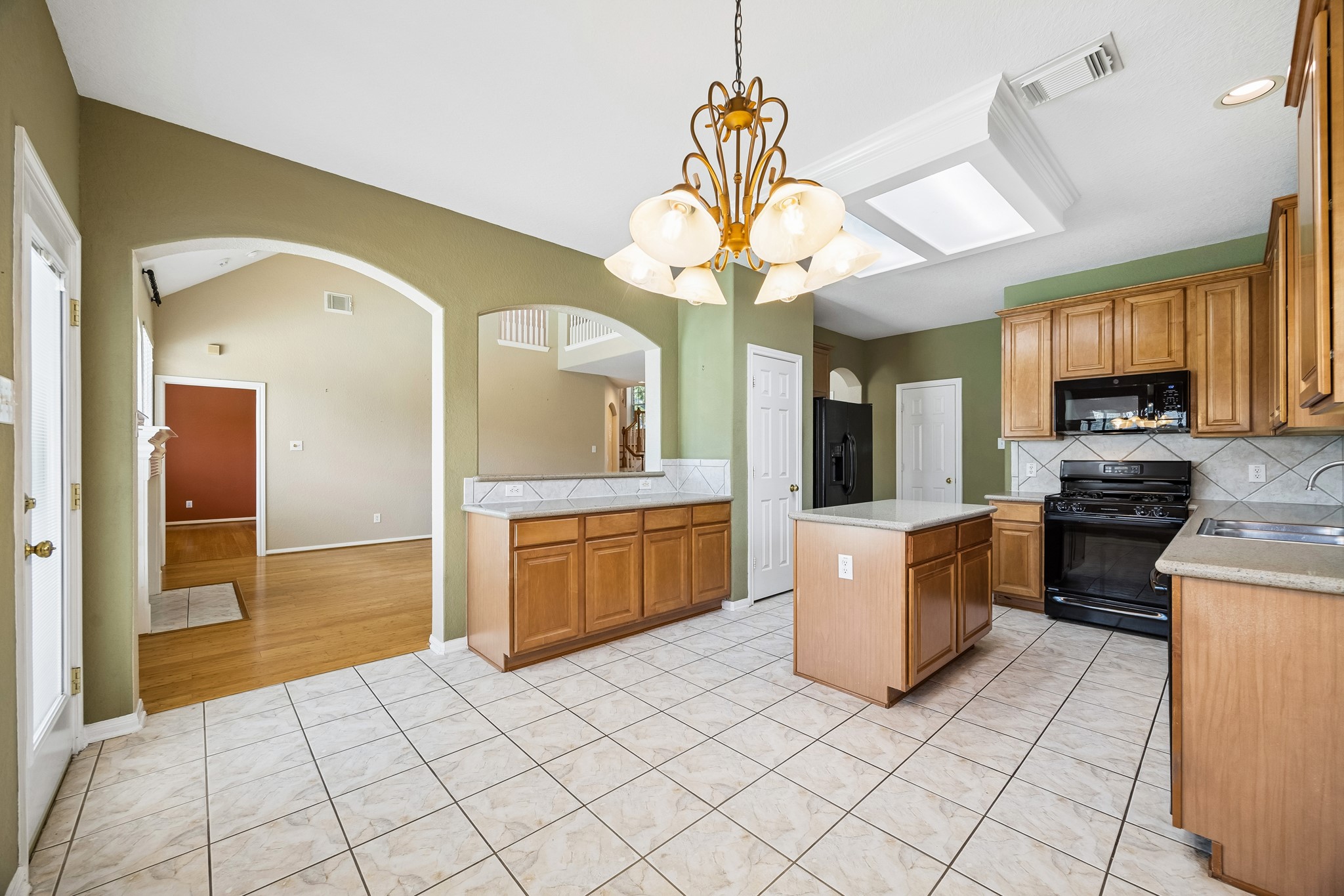 Arched openings and the pass-through bar keep the kitchen connected to the family room, while quartz counters, classic cabinetry and bright overhead lighting make the space both practical and welcoming.