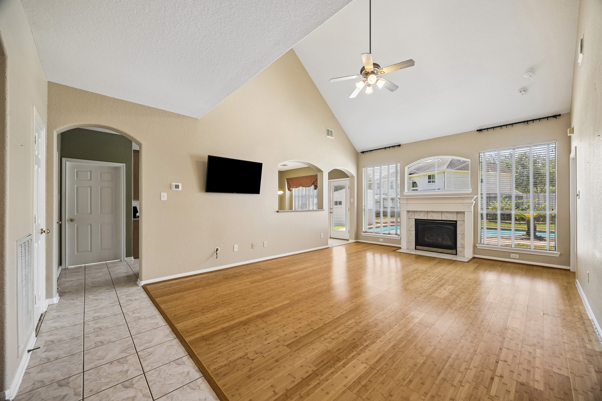 A gas log fireplace creates a cozy focal point while large windows bring the sparkling backyard pool right into view. A convenient pass through bar to the kitchen and the arched window above the fireplace add unique architectural touches and a little extra character to the space.