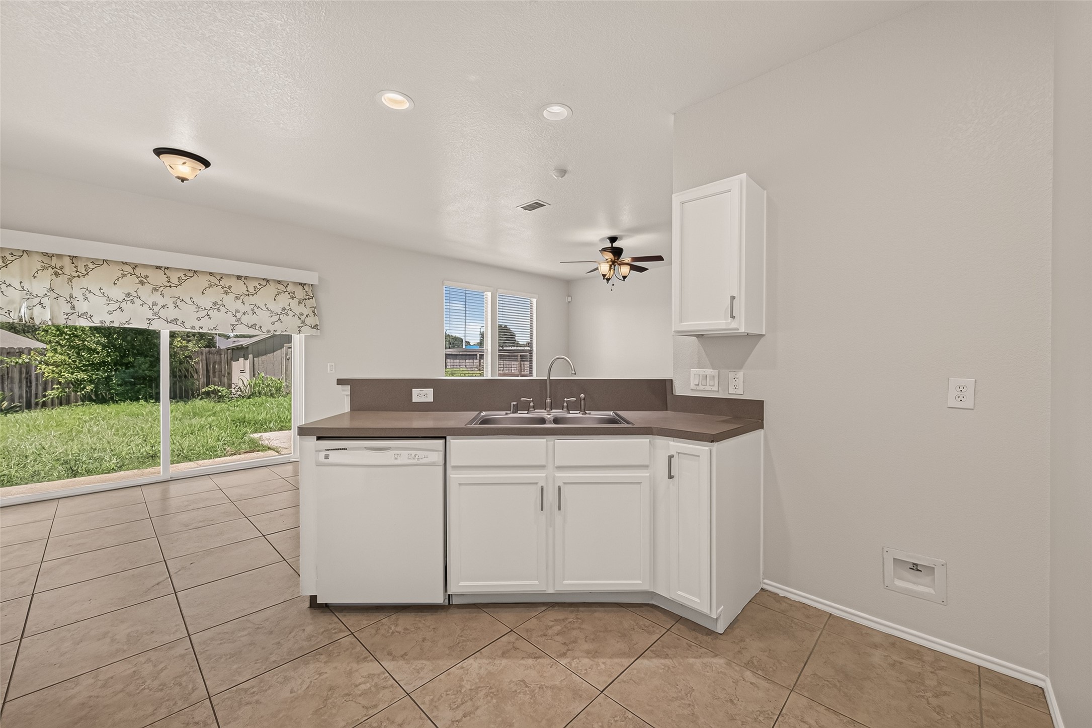 This photo showcases a backyard with a patio area featuring sliding glass doors, a small bench, and well-maintained grass. A wooden fence offers privacy, and a shed provides extra storage space.