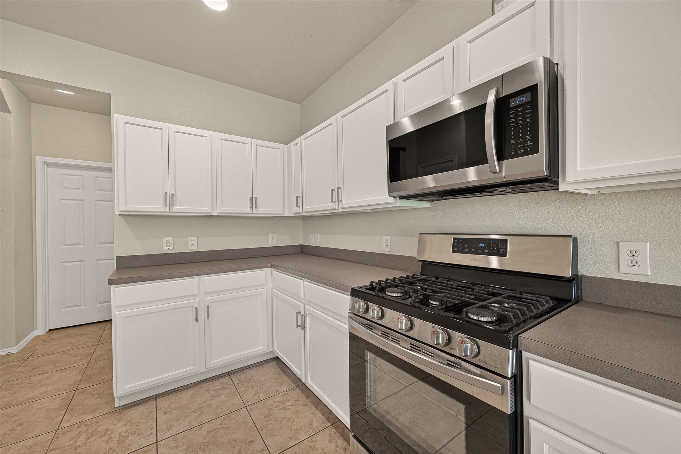 This spacious kitchen features modern stainless steel appliances, sleek white cabinetry, and ample counter space. It opens to a bright area with windows, providing a welcoming and functional layout.