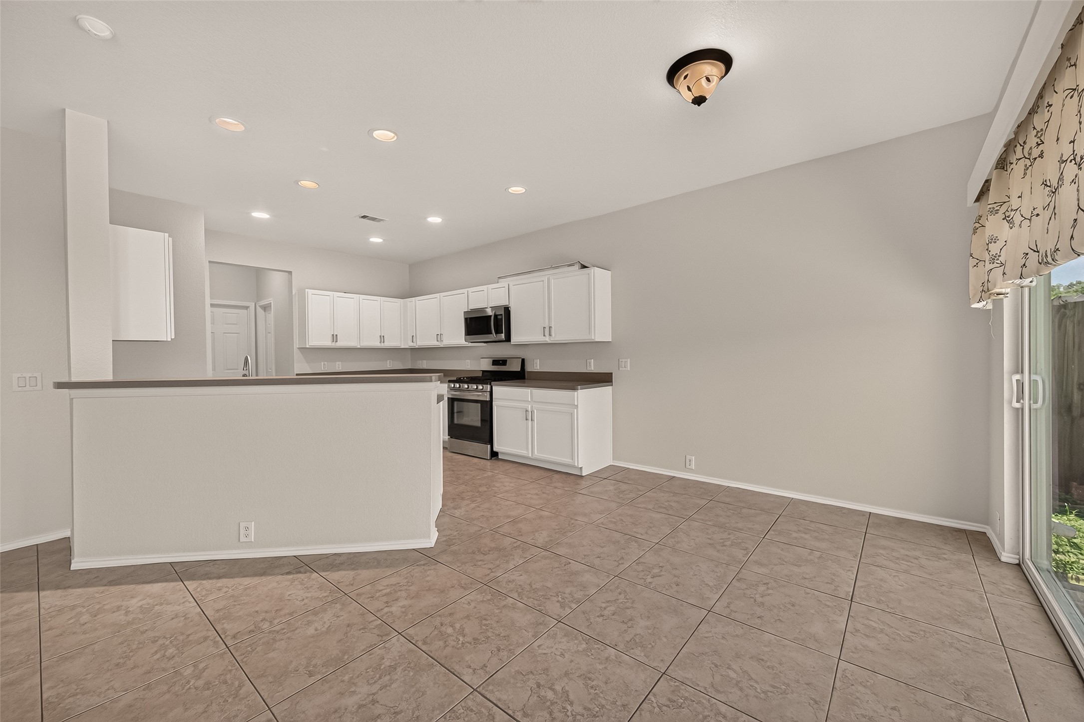 This spacious kitchen features modern appliances, ample white cabinetry, and a large countertop area. The open layout connects to a tiled dining area with plenty of natural light from sliding glass doors.