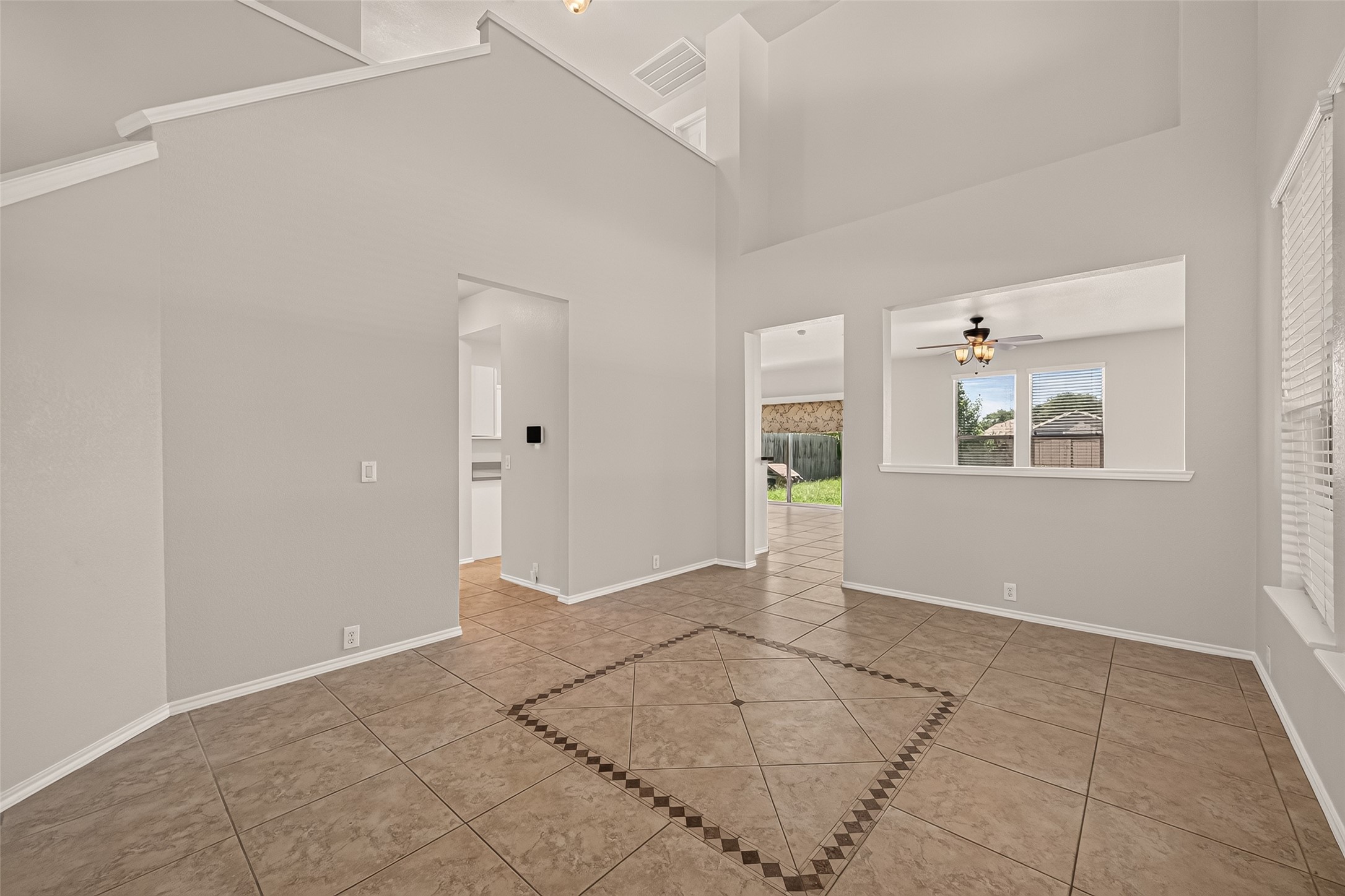 This spacious room features high ceilings and large windows, creating a bright and airy atmosphere. The tiled floor adds a modern touch, and there's a view into the backyard, offering a seamless indoor-outdoor connection.
