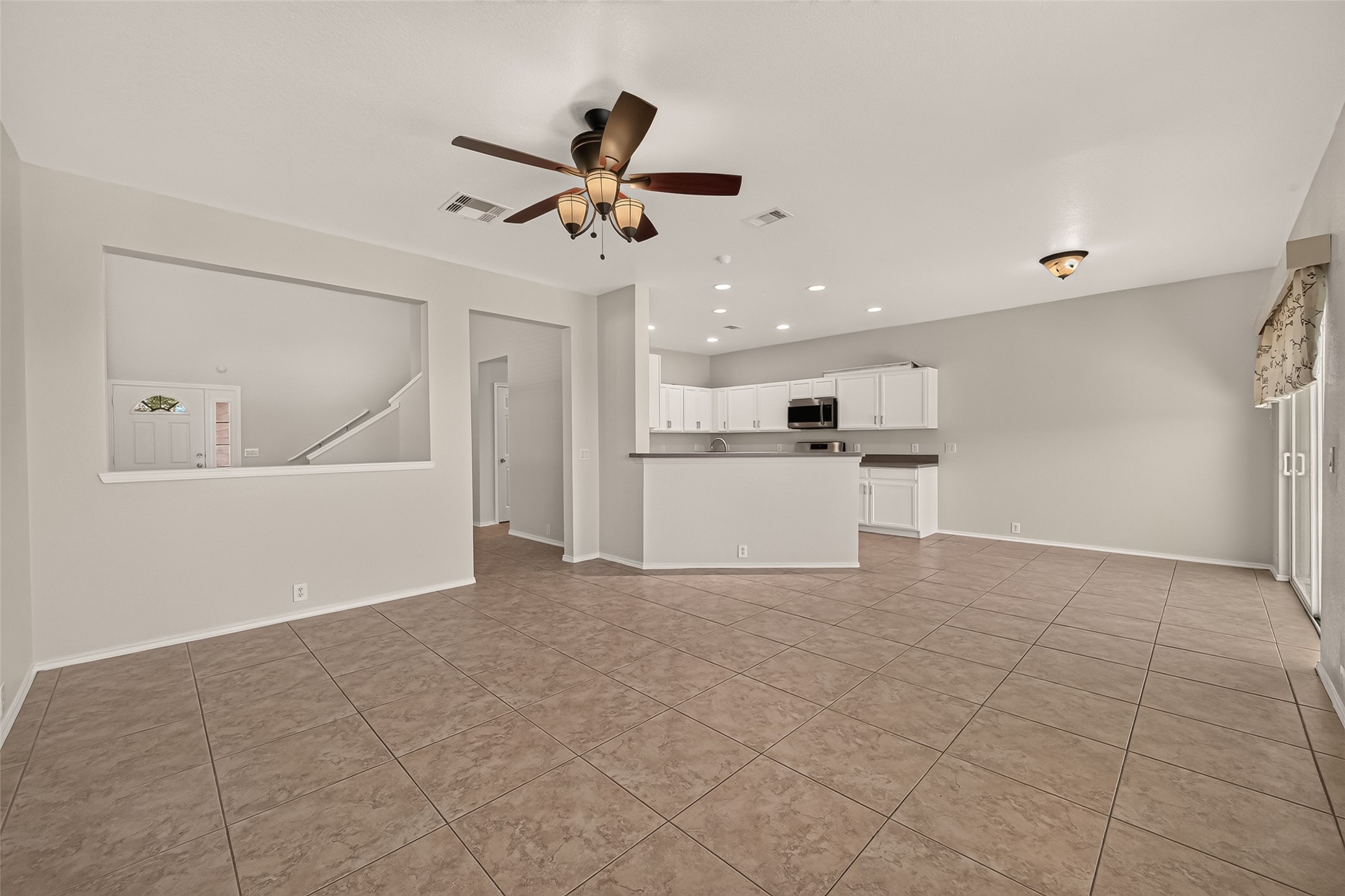 This spacious open-concept living area features a tiled floor, ceiling fan, and ample natural light. It seamlessly connects to a modern kitchen with white cabinetry and a breakfast bar, perfect for entertaining.